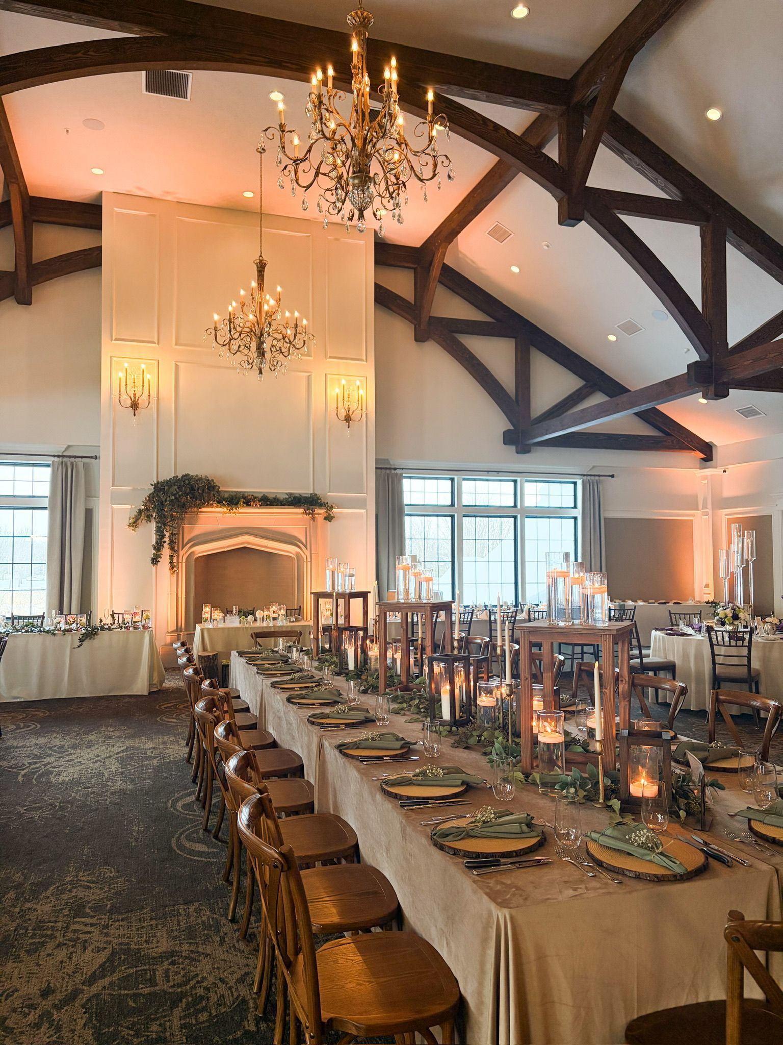 Elegant reception hall with long table set for a wedding, featuring chandeliers, candles, and floral arrangements.