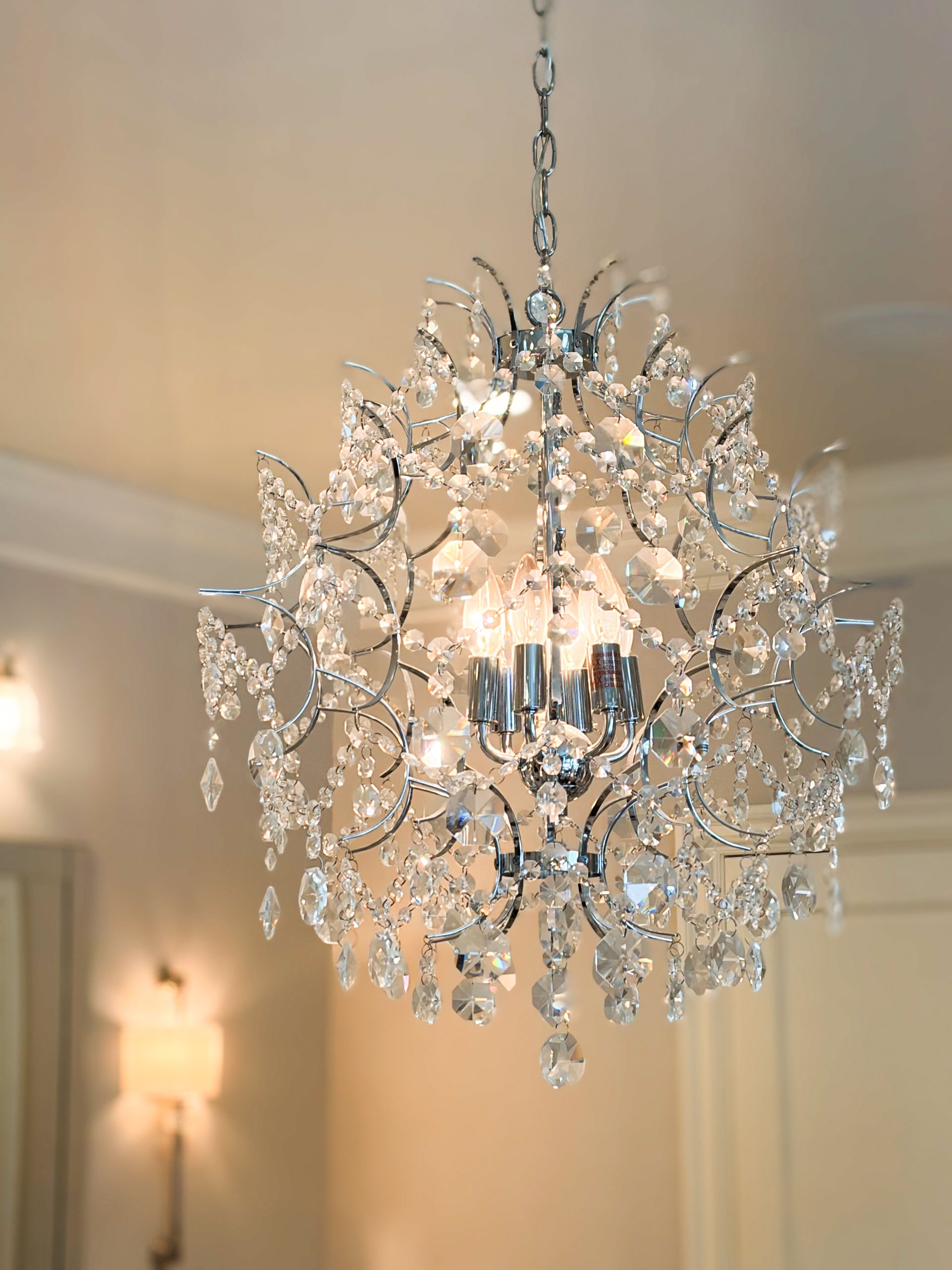 Crystal chandelier hanging from ceiling, chrome finish, sparkling lights.