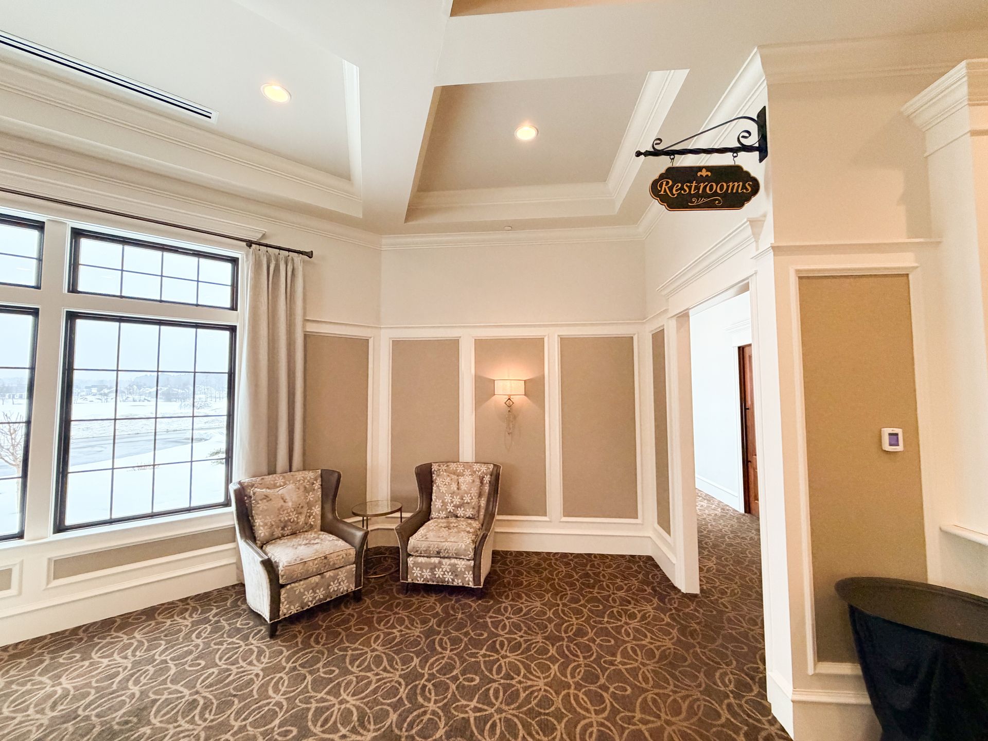 Elegant waiting area with two patterned armchairs, window, and sign.