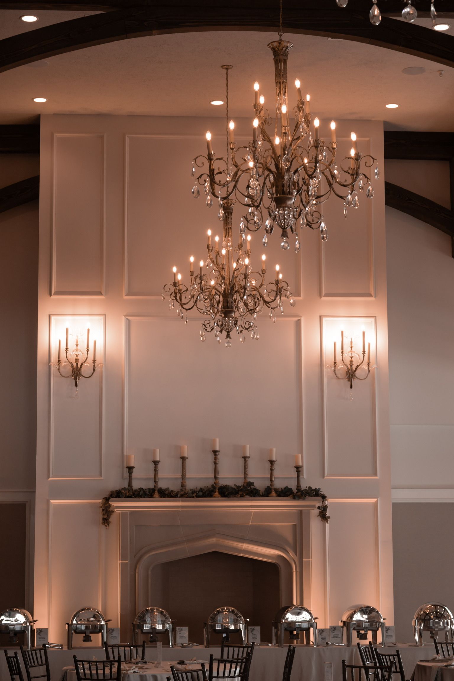 Elegant ballroom with chandeliers, fireplace, and tables set for an event. Warm lighting.