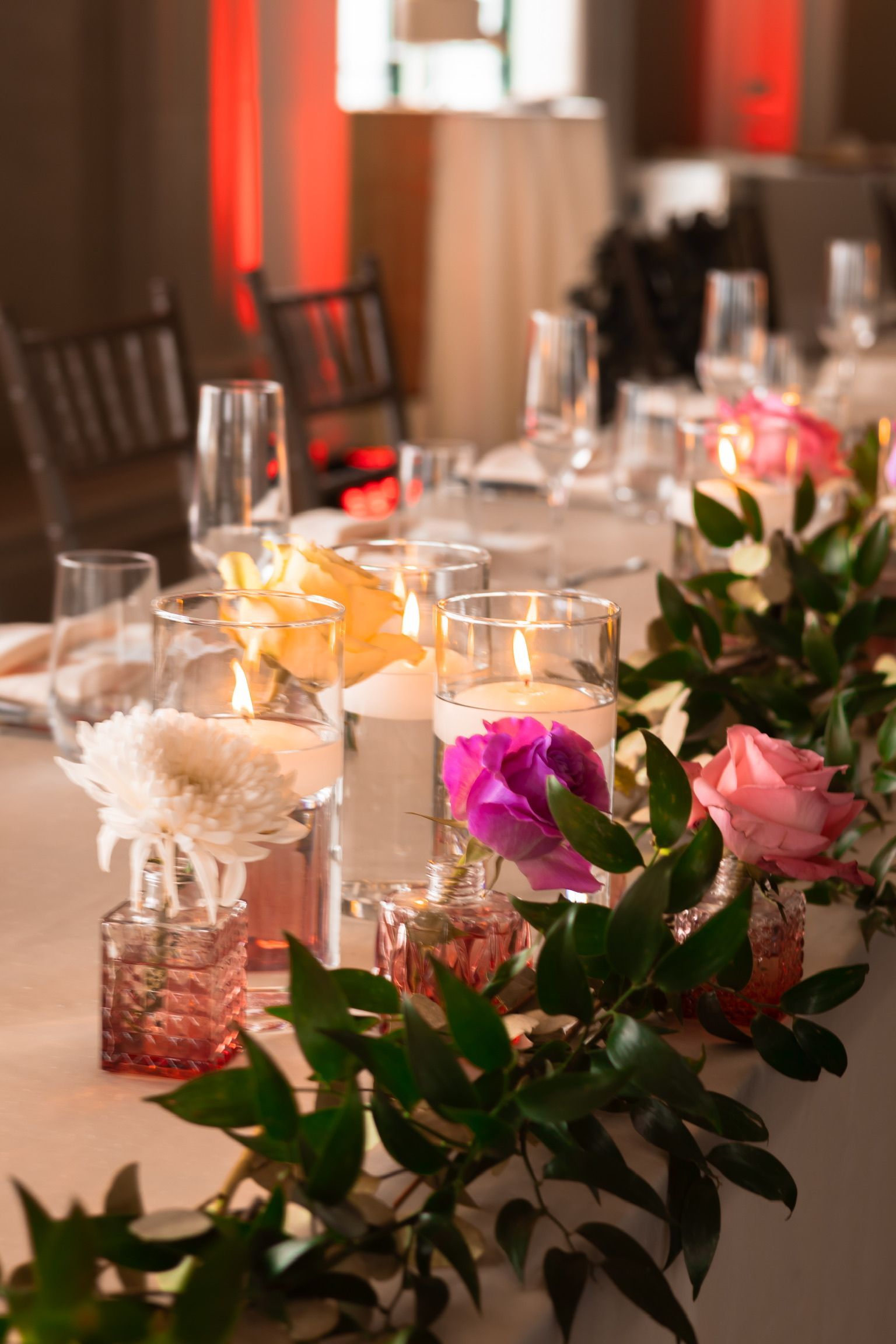 Table setting with flowers, candles, and greenery, in a room with a white tablecloth.