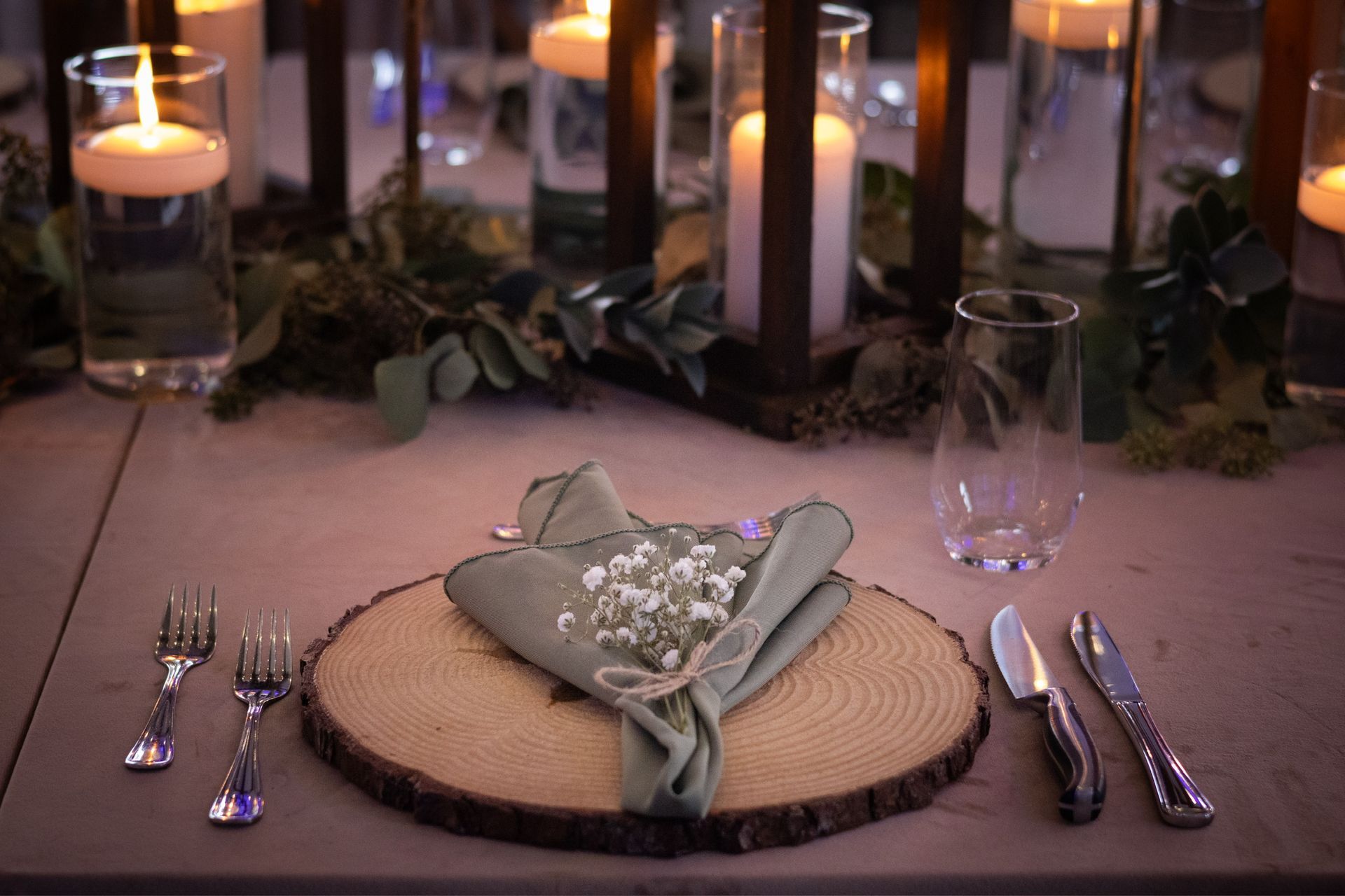 Table setting with wooden charger, green napkin, silverware, and candles.