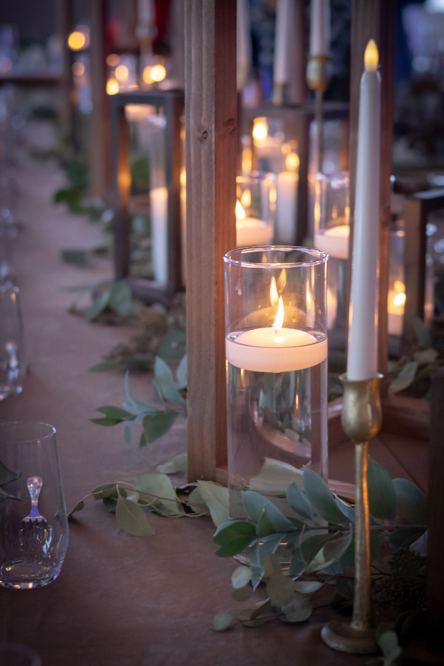 Table centerpiece with candles in glass and wooden holders, greenery garland.
