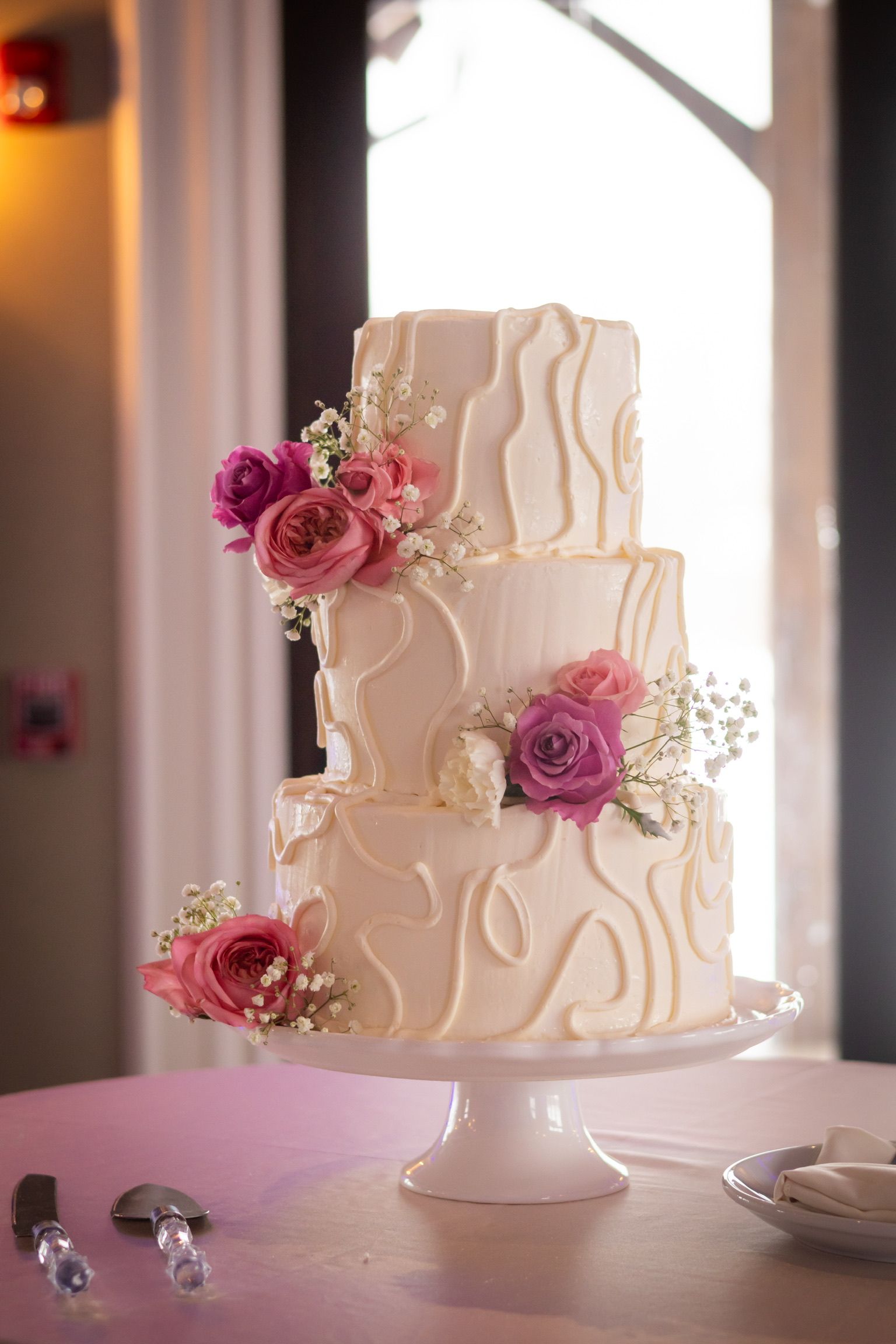 Three-tiered white cake with pink flowers on a white cake stand.