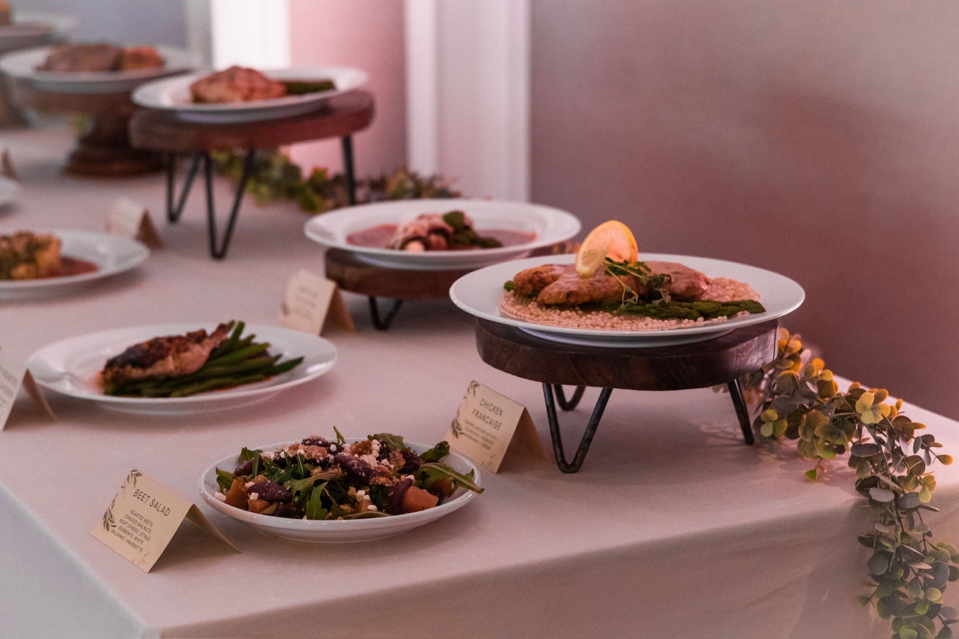 Buffet table with various dishes on elevated stands, including meat, vegetables, and salad.