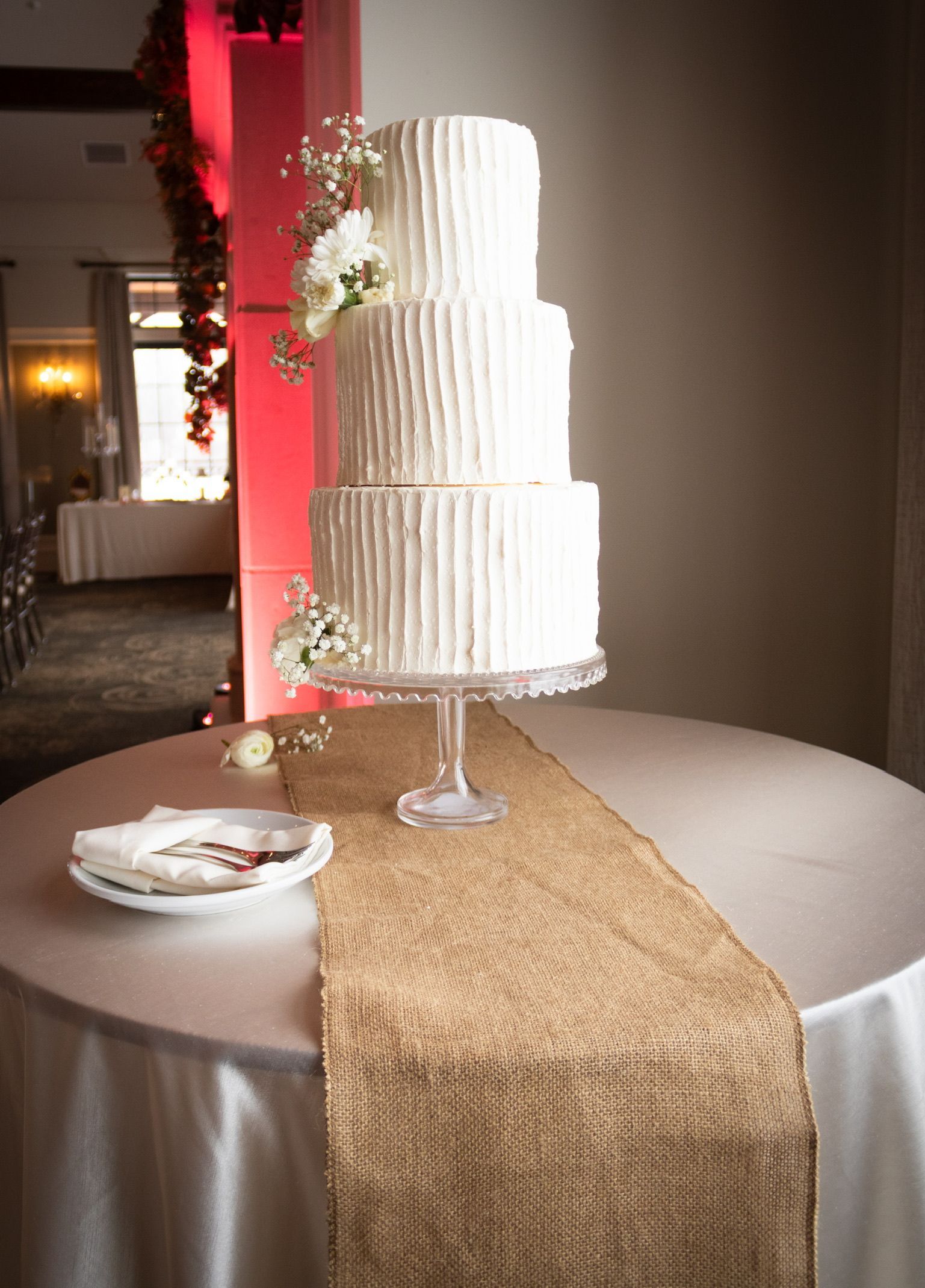 Three-tiered white wedding cake with floral accents on a table with a gold runner.