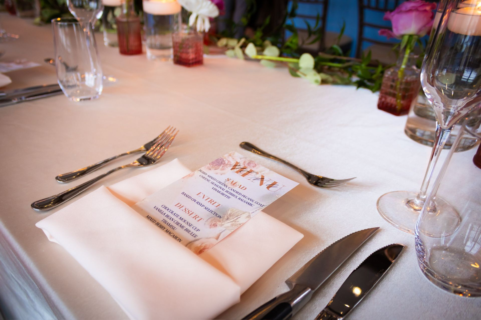 Formal table setting with folded napkin, menu, silverware, and floral centerpieces.