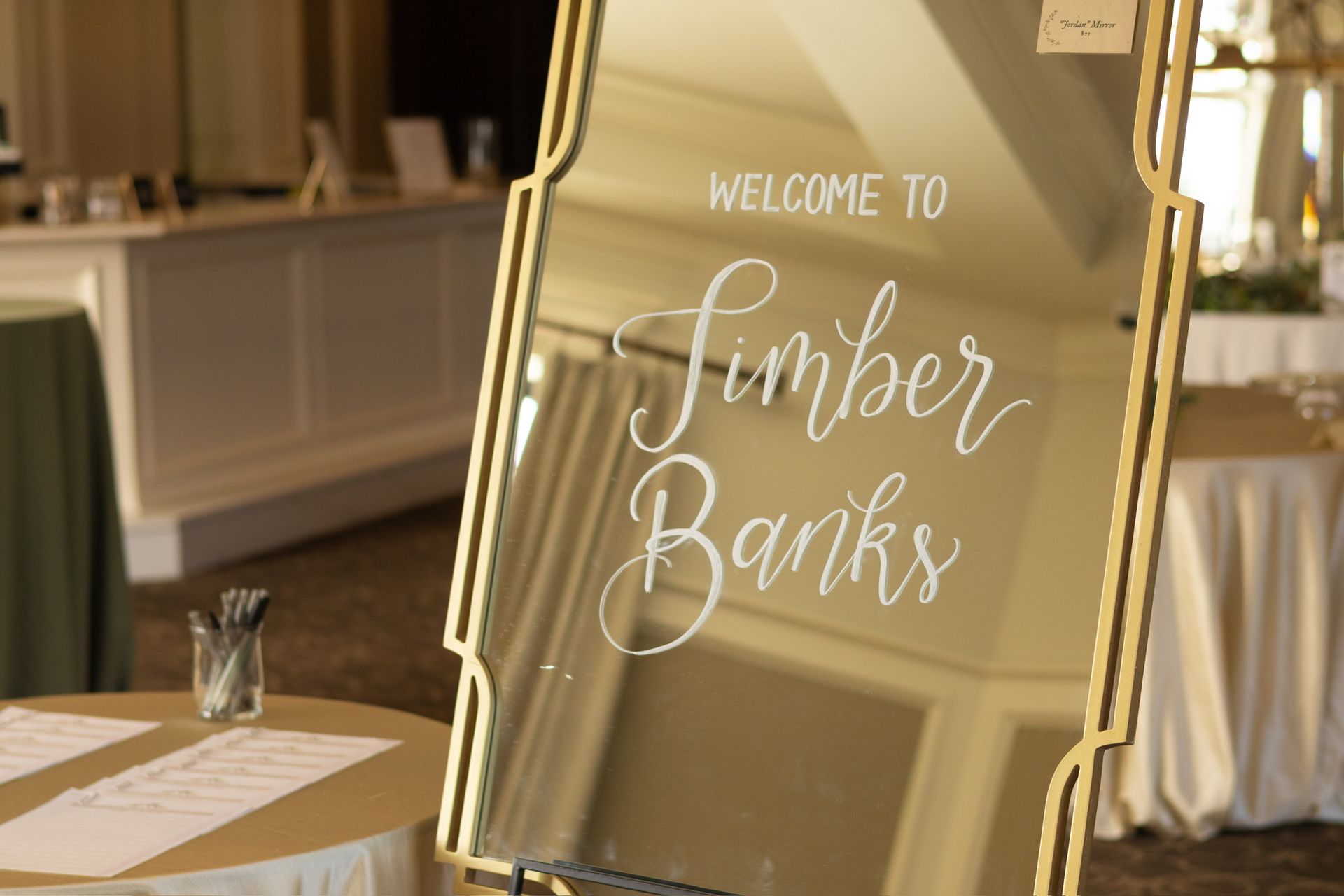 Mirror sign welcoming guests to Timber Banks, with gold frame, script lettering, and a table with guest book.