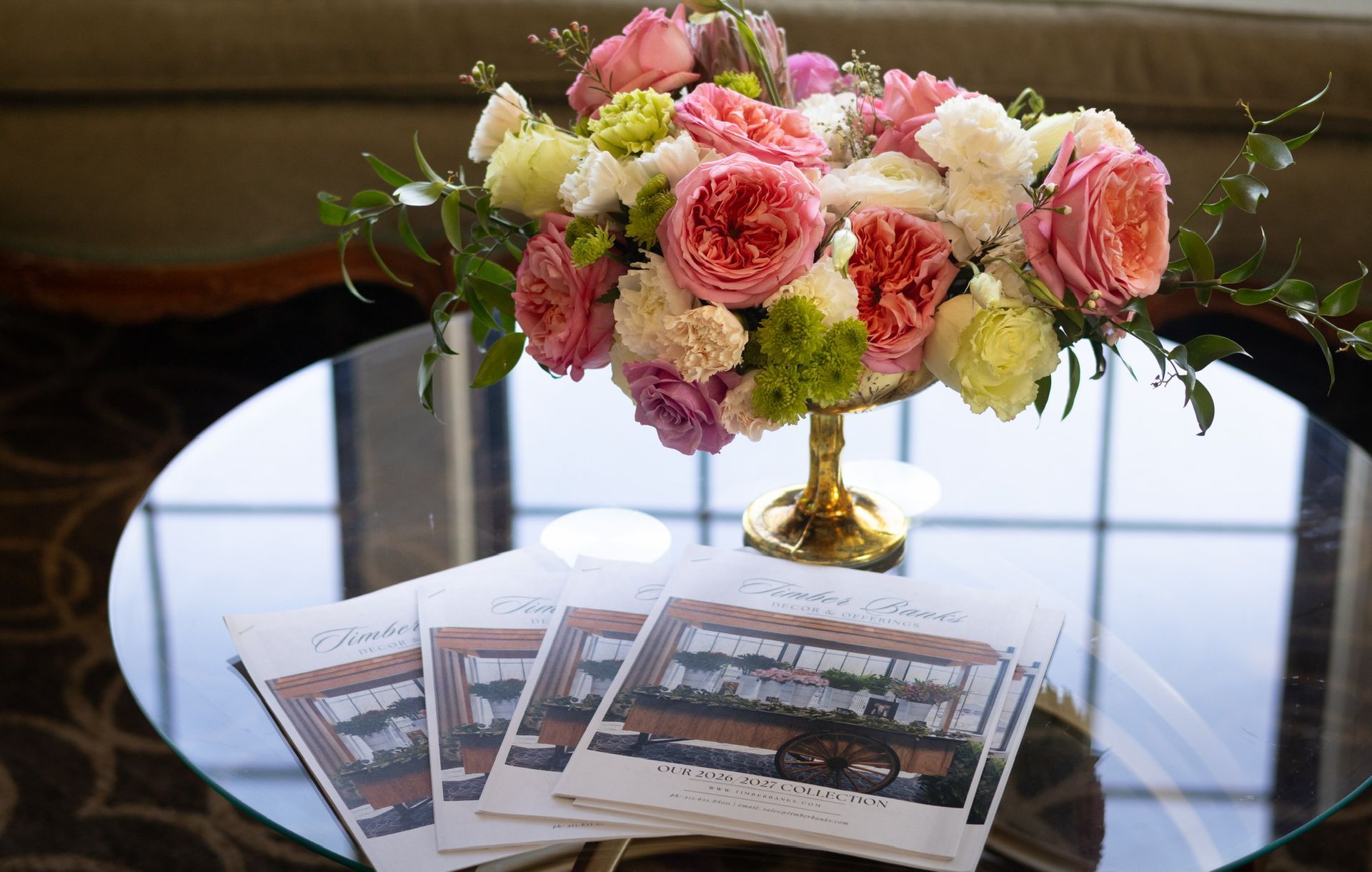 Bouquet of pink, coral, and white flowers in gold vase atop a table with brochures.