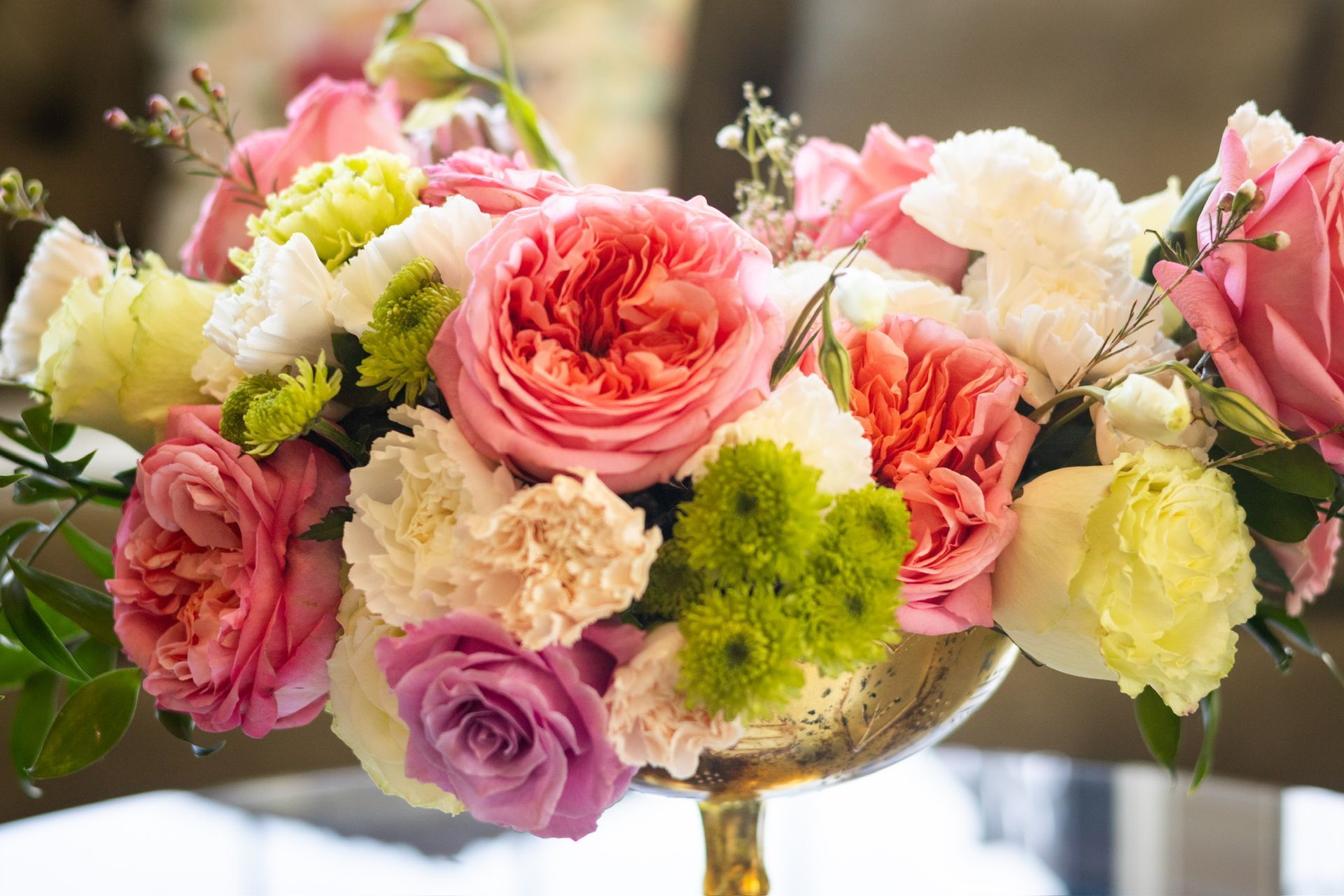 Close-up of a floral arrangement in a gold vase; pink roses, white carnations, and green and yellow flowers.