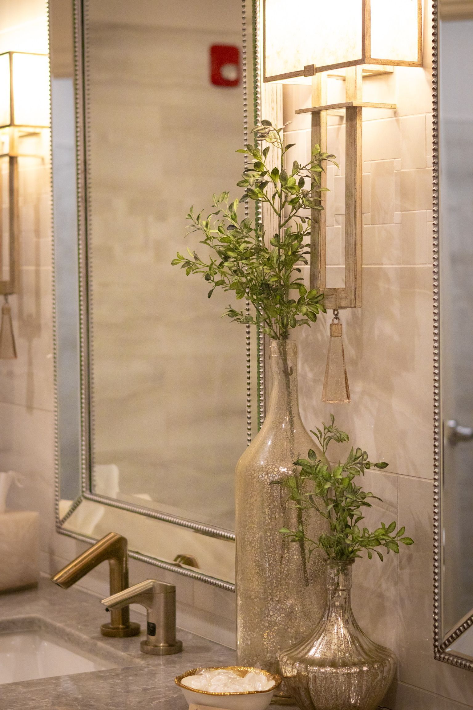 Bathroom vanity with gold fixtures, two decorative vases with greenery, and a mirror.