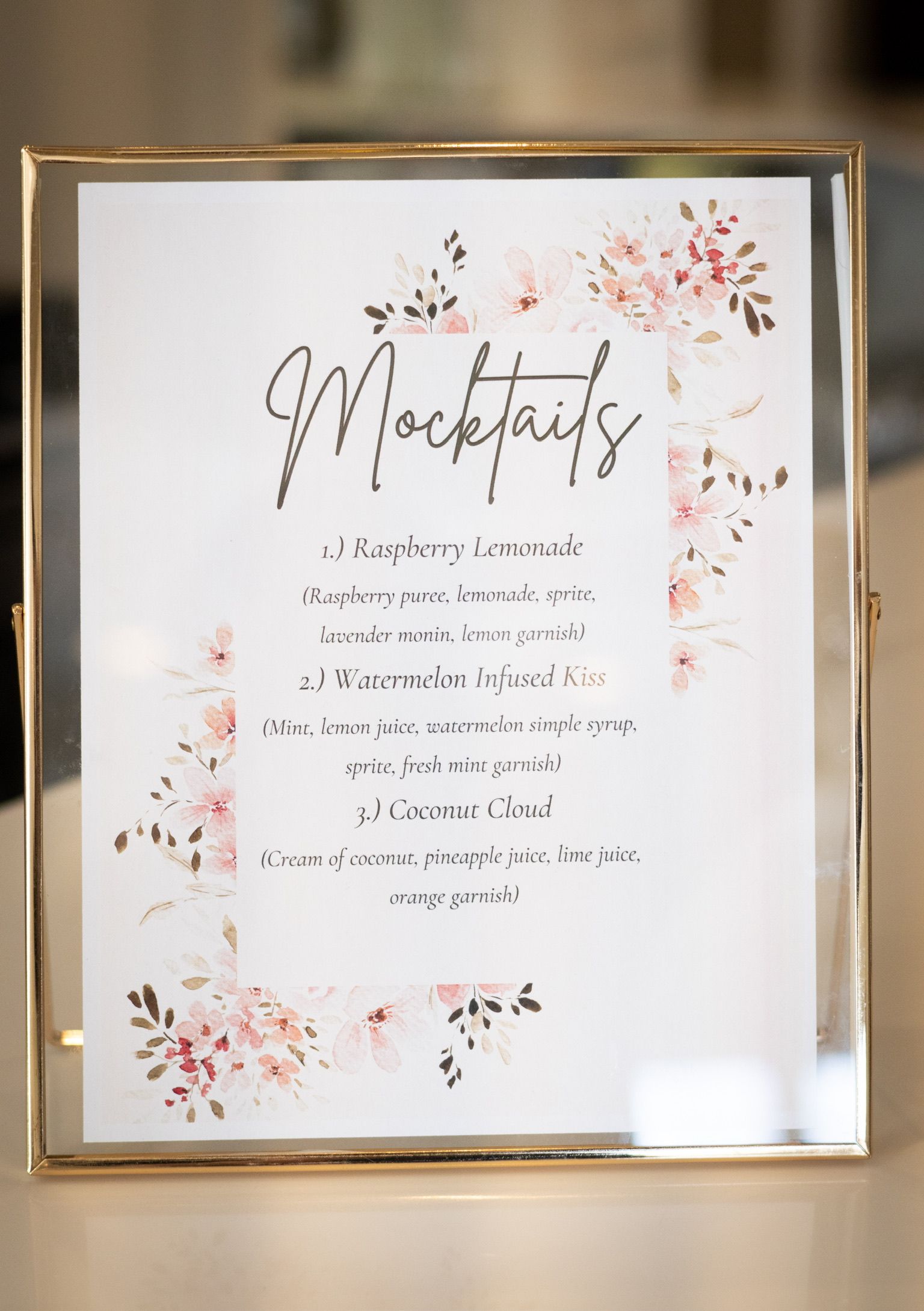 Mocktails menu sign in a gold frame, decorated with pink floral accents.