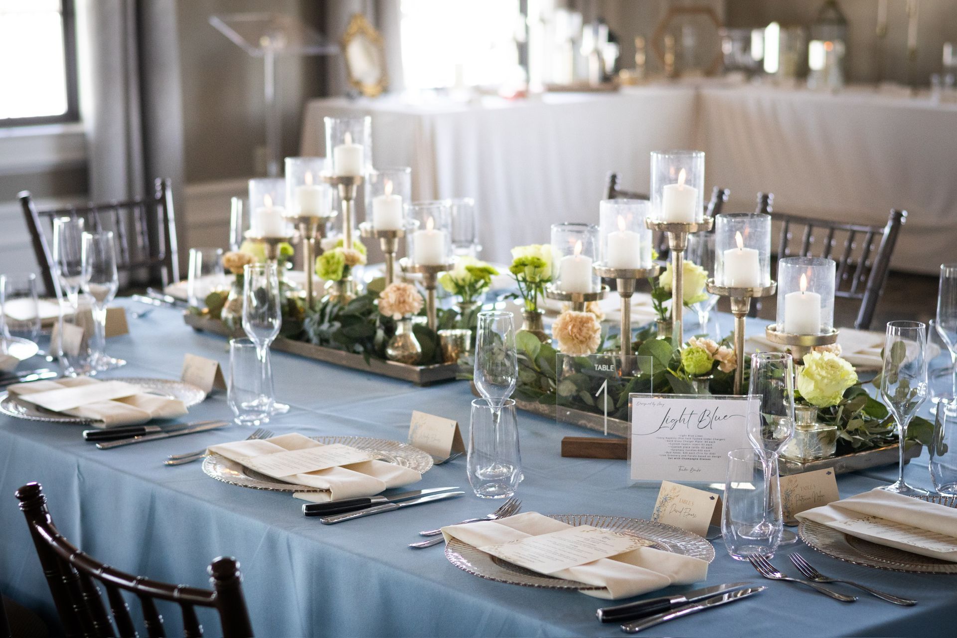 Formal table setting with blue tablecloth, floral centerpiece, and gold candle holders.