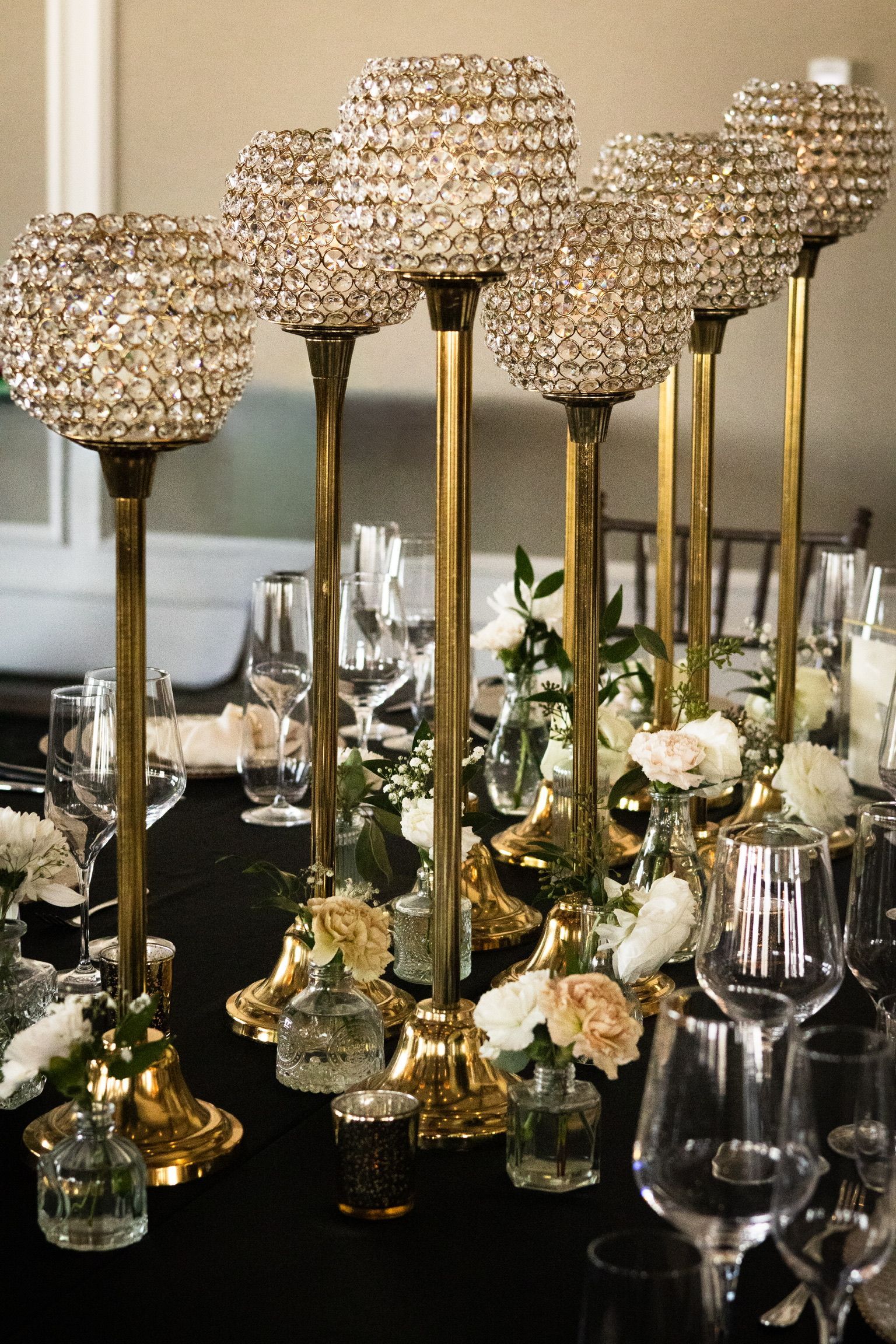 Elegant table setting with gold candelabras, crystal orbs, flowers, and glassware on a black tablecloth.