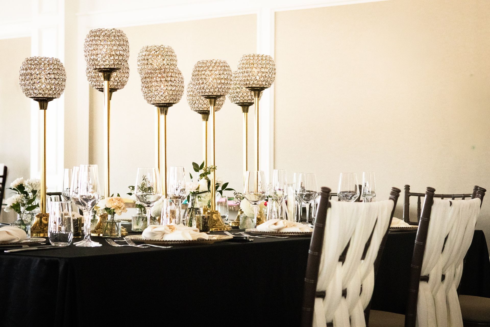 Formal dining table set with gold candle holders and white chair decor.