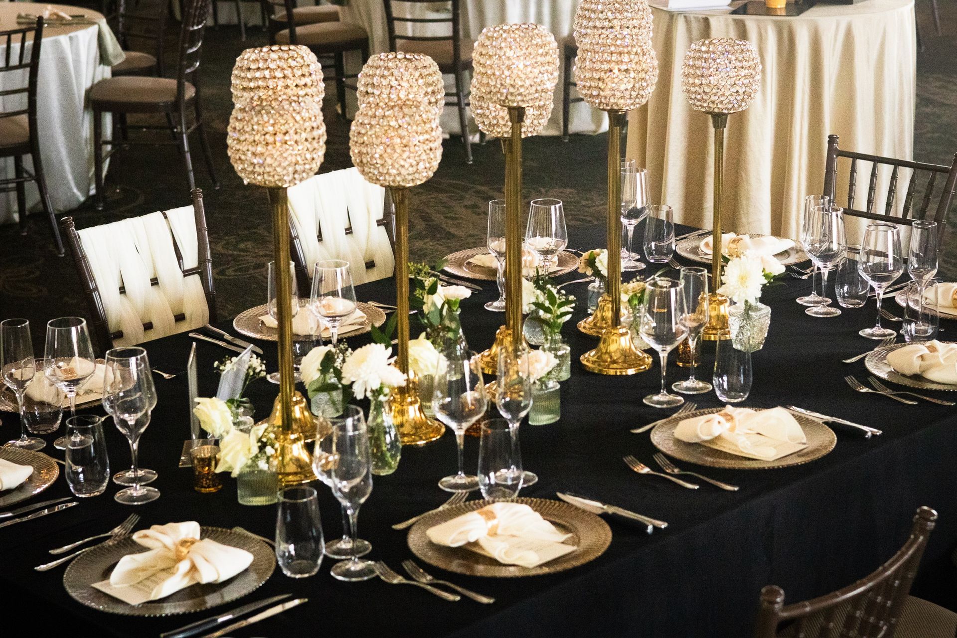 Formal dinner table set with gold beaded candle holders and black tablecloth.