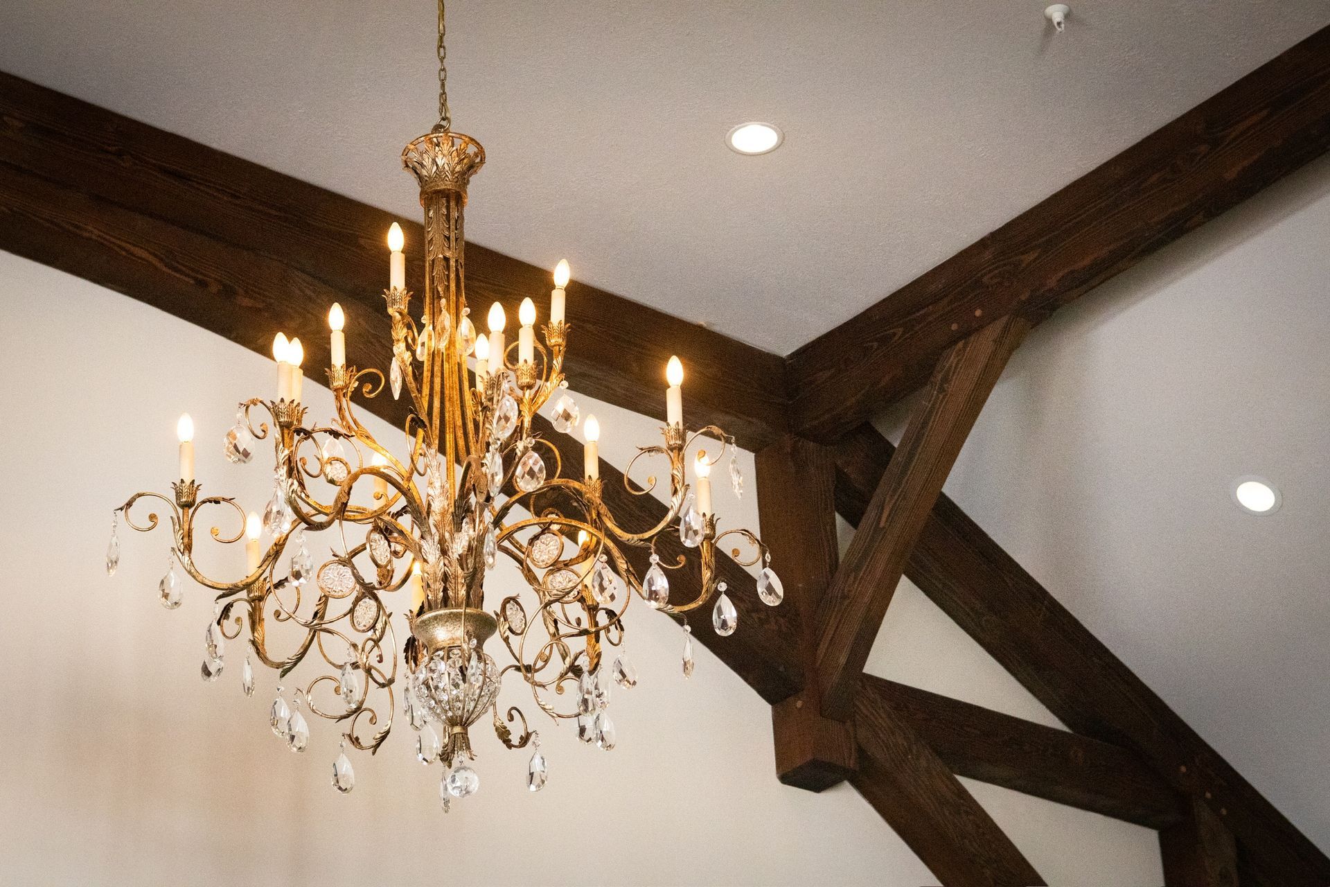 Ornate chandelier hanging from dark wooden beams. White ceiling with recessed lights.