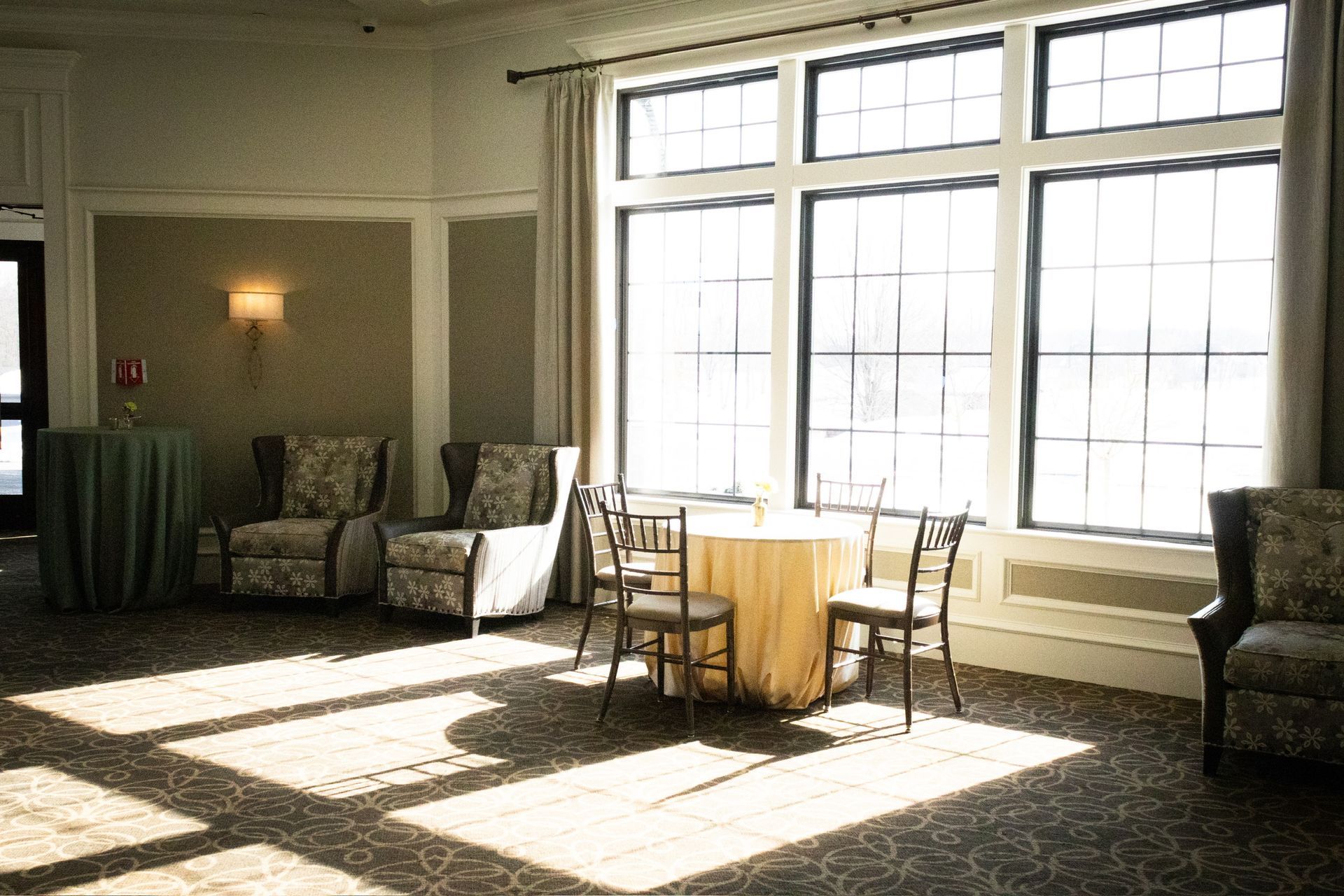 Sunlit room with table and chairs near large windows, and seating area with armchairs.