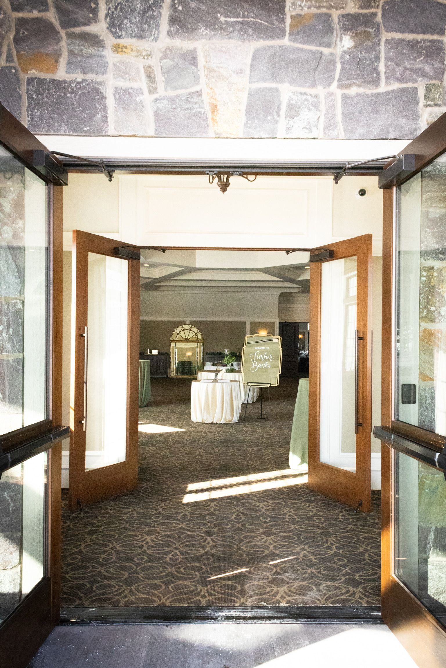 Open wooden doors leading into a well-lit reception hall, beige carpet, and decorative tables.