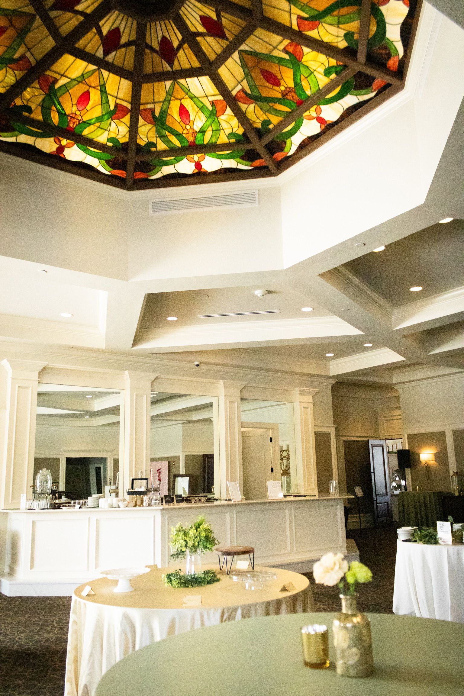 Elegant event space with a stained glass ceiling, round tables, and a bar.