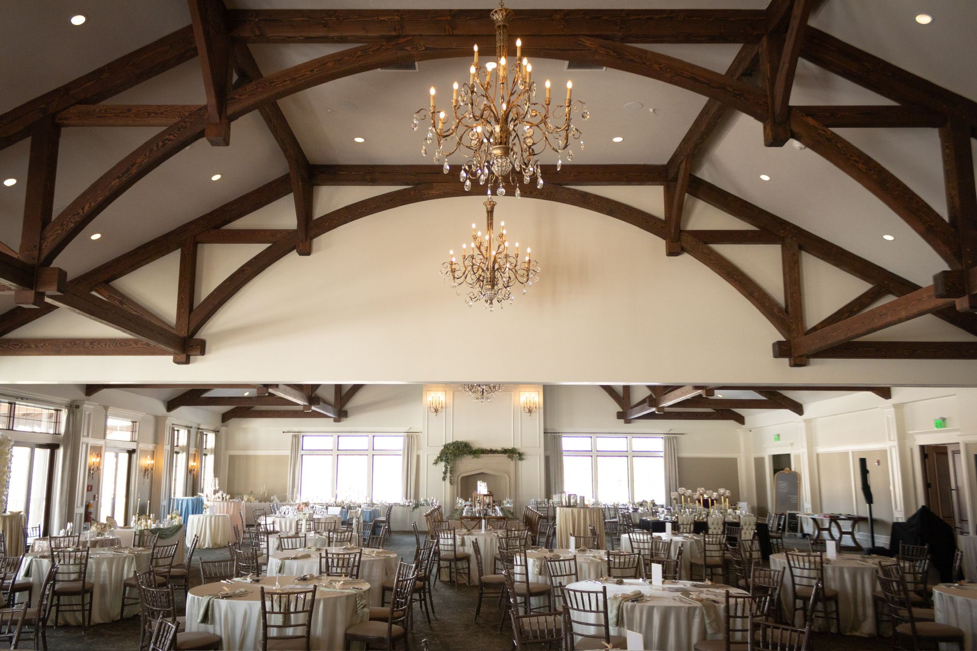 Banquet hall with tables set for a reception. Wooden beams and chandeliers adorn the ceiling.