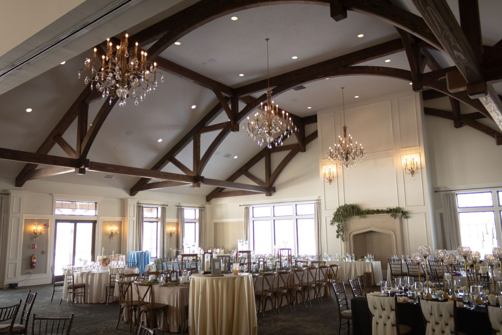 Elegant event hall with chandeliers, wooden beams, tables set for dining.