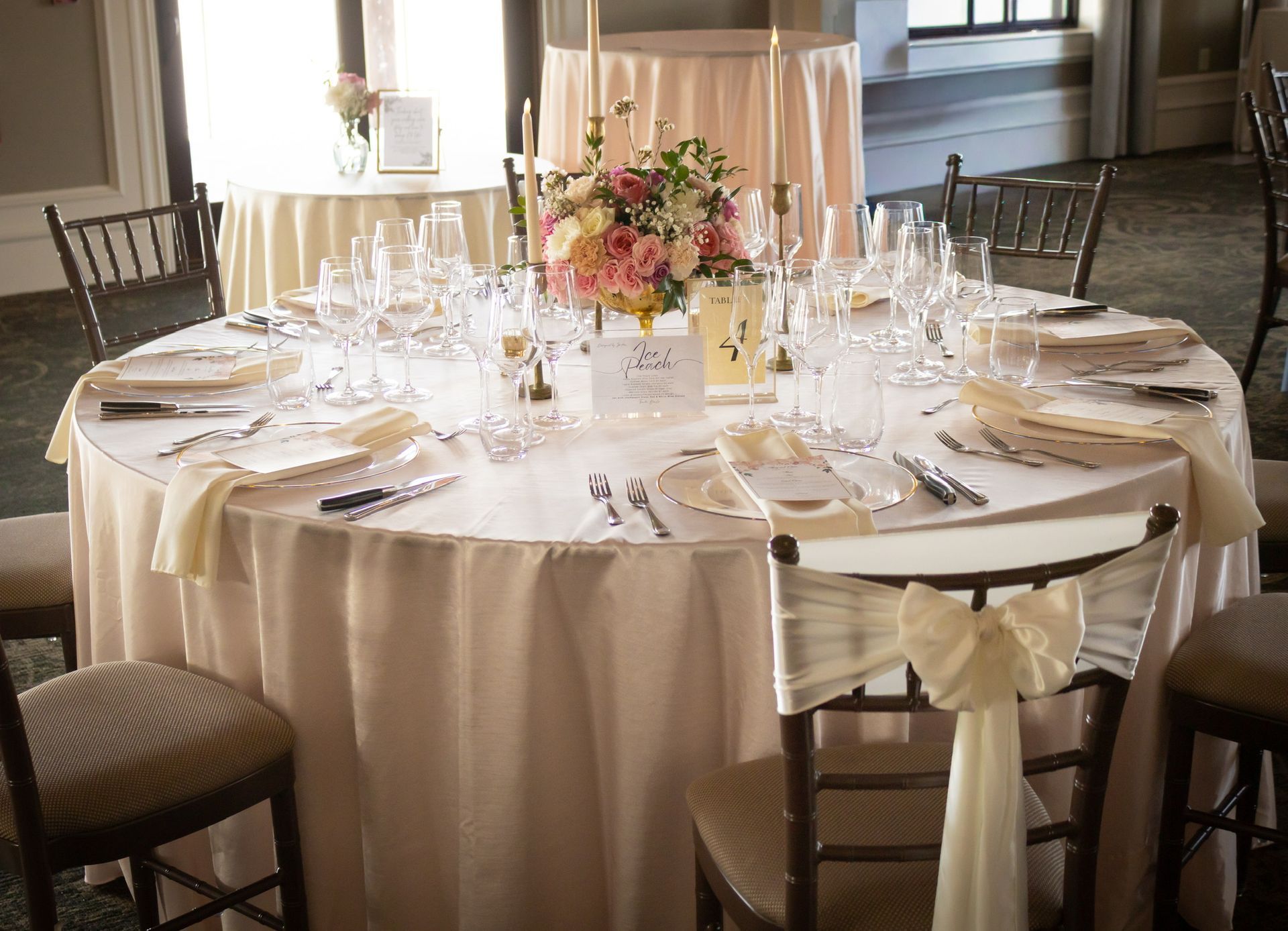 Round table set for a formal event, cream tablecloth, flower centerpiece, place settings, and chairs.
