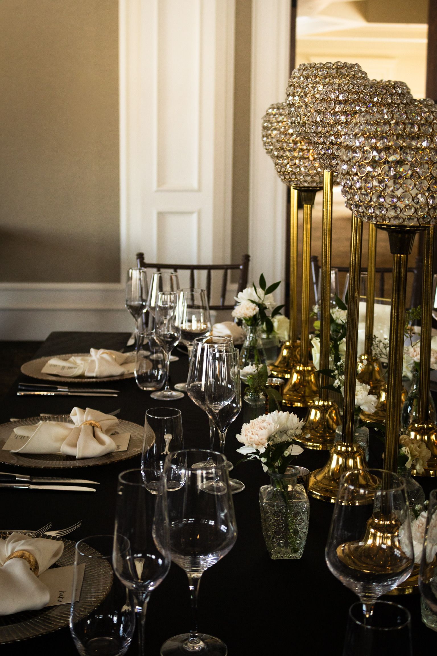 Elegant table setting with black tablecloth, gold accents, crystal decor, and glassware.