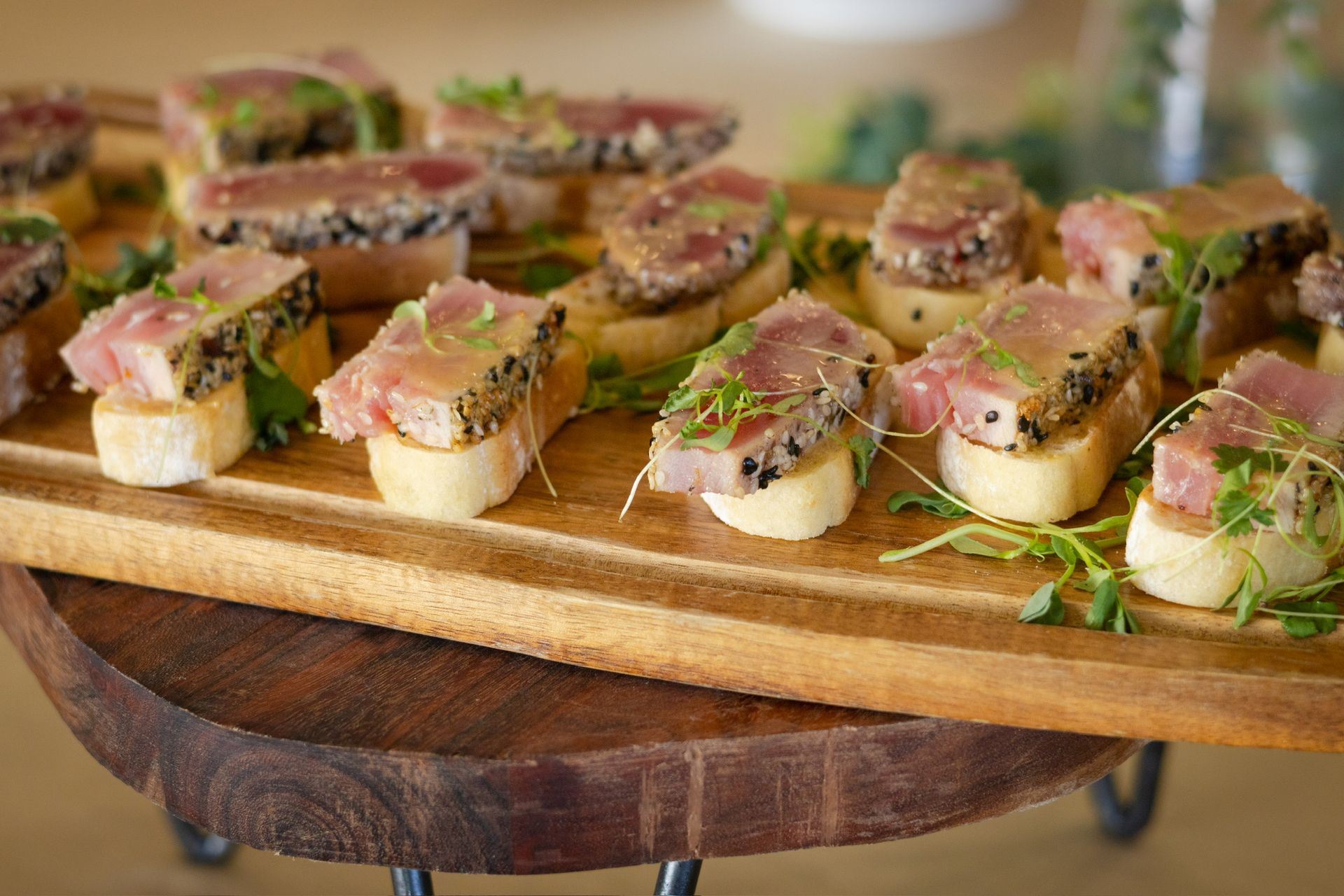 Seared tuna appetizers on toasted bread, served on a wooden platter.