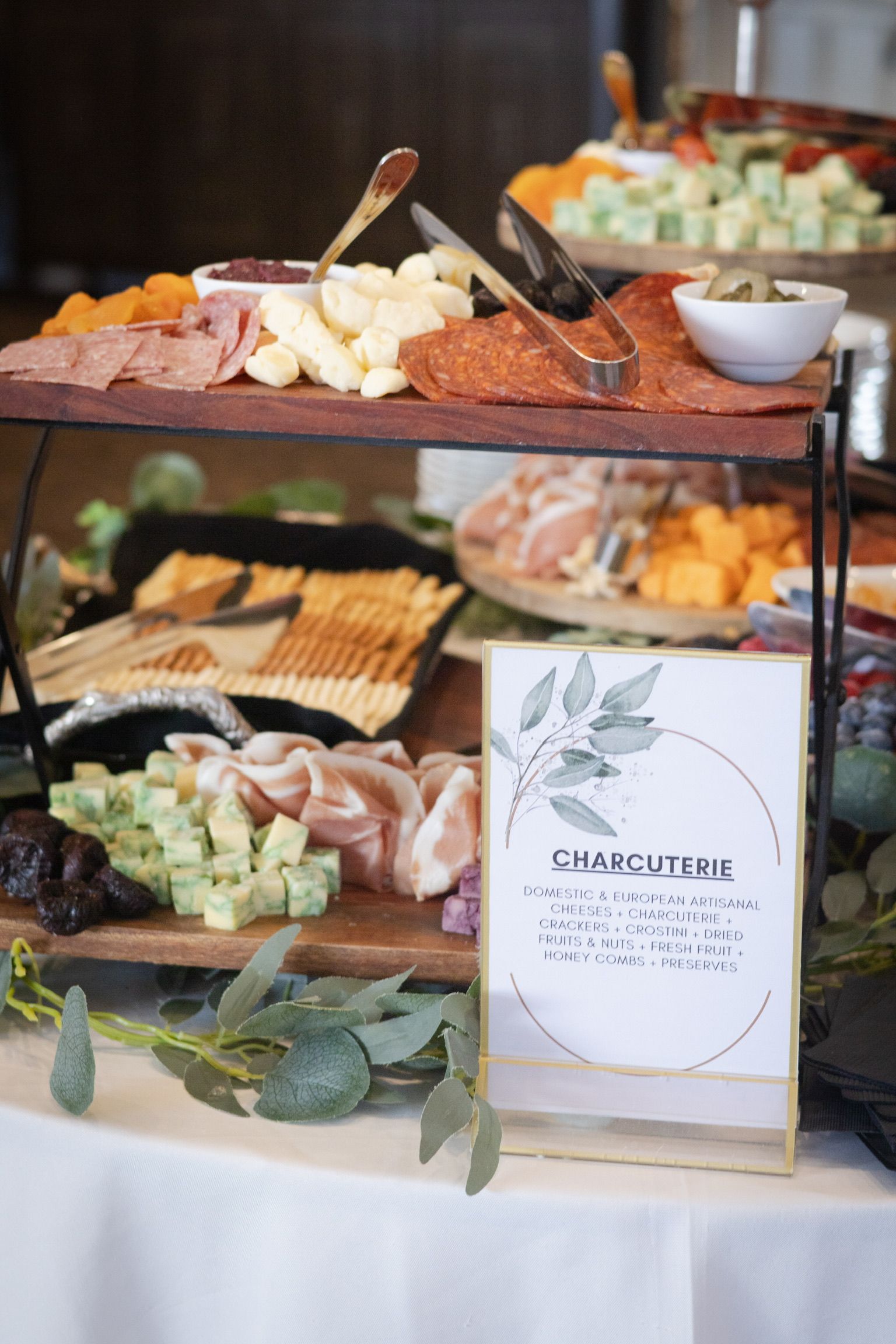 Charcuterie board with cheeses, meats, crackers, and fruit on tiered wooden serving platters.