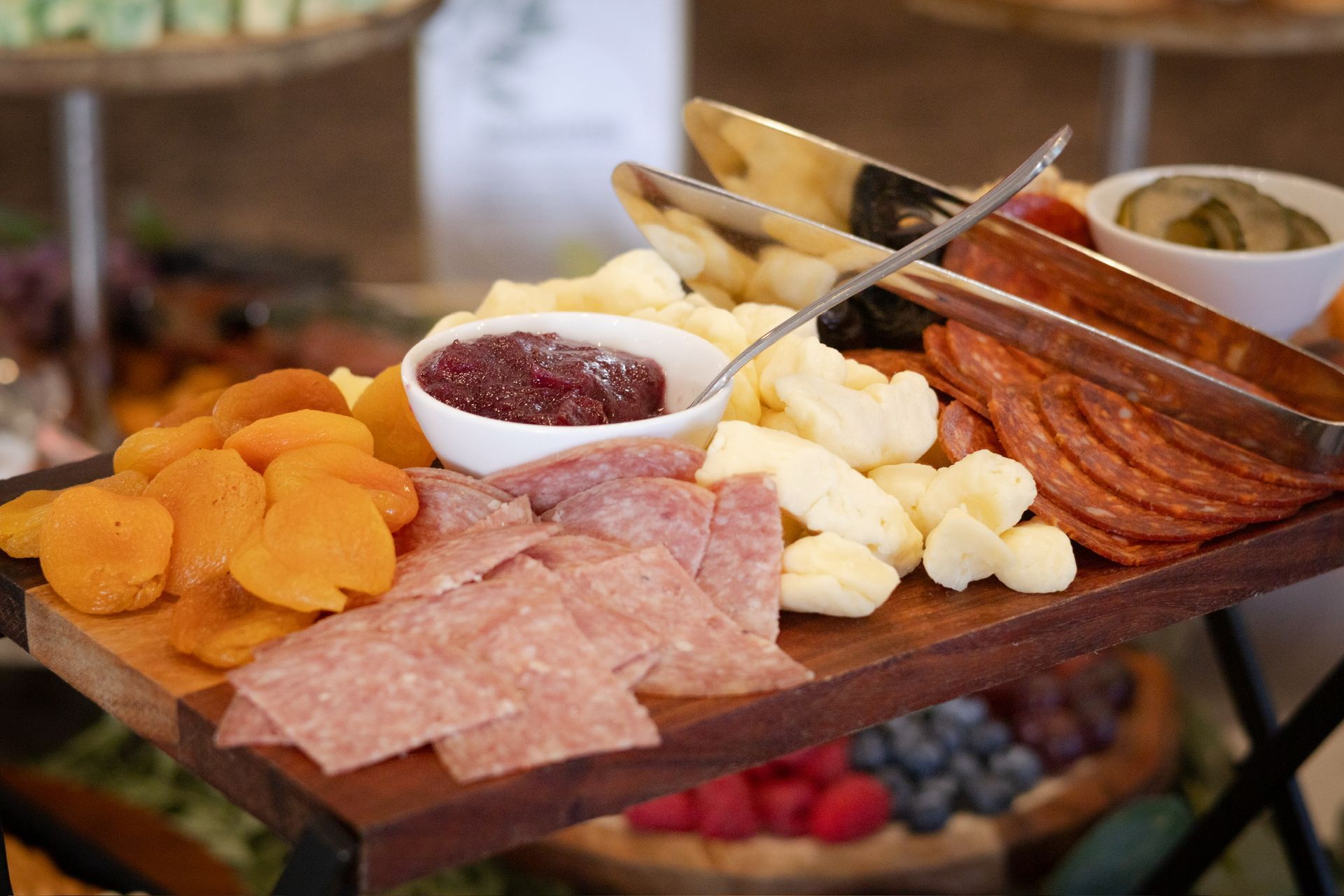 Wooden charcuterie board with sliced meats, cheeses, dried apricots, and jam.