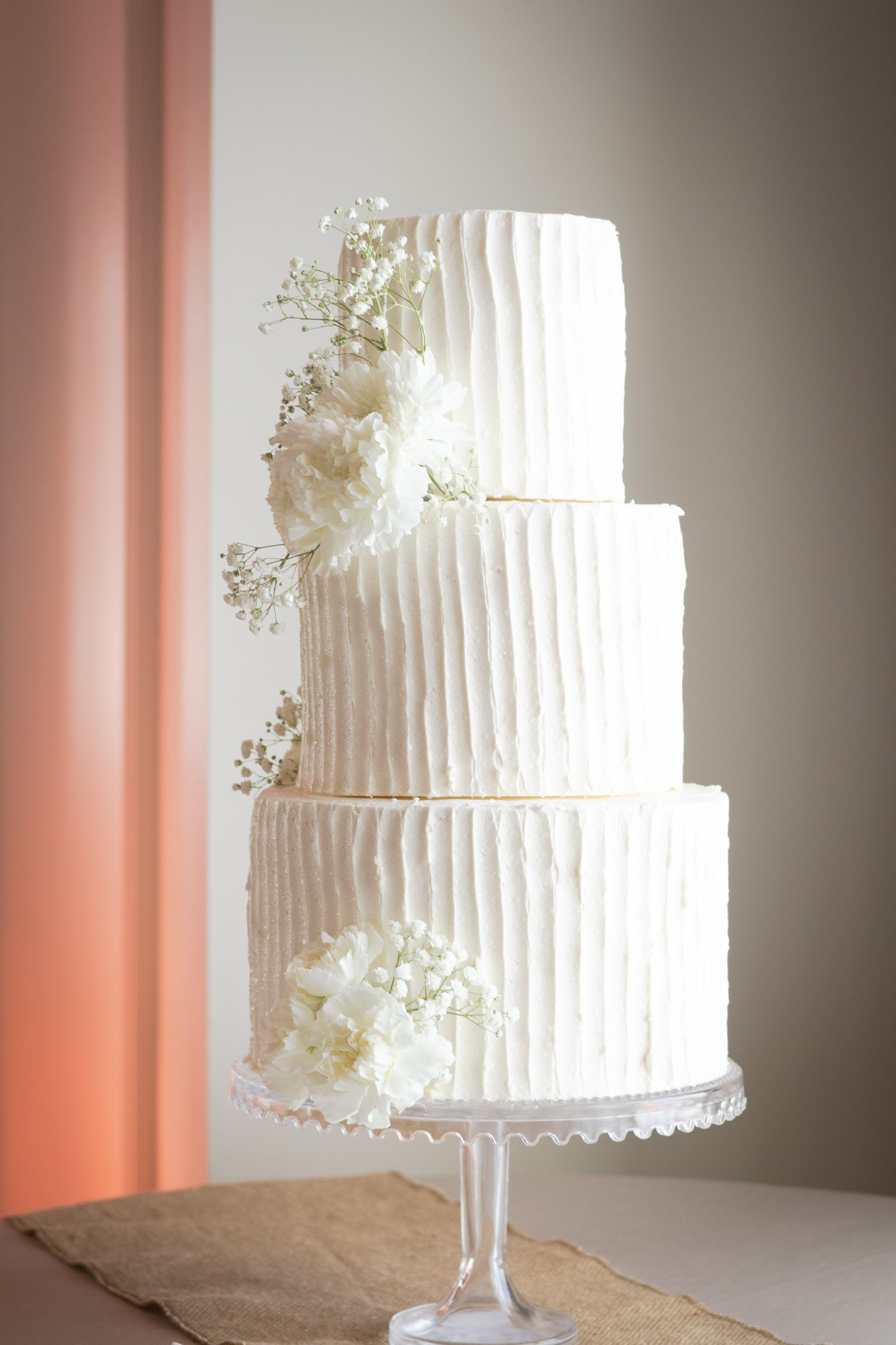 Three-tiered white cake with textured frosting and floral decorations on a glass cake stand.