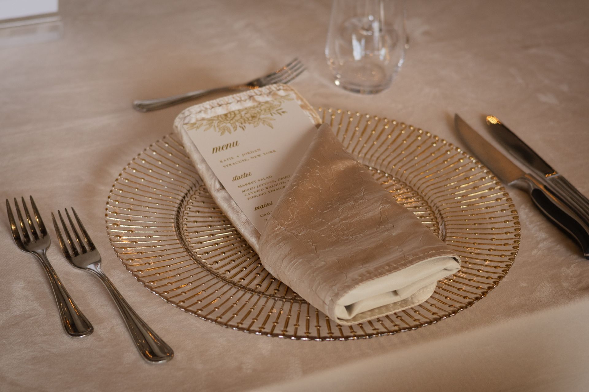 Place setting with gold charger, napkin, menu, silverware, and glass.