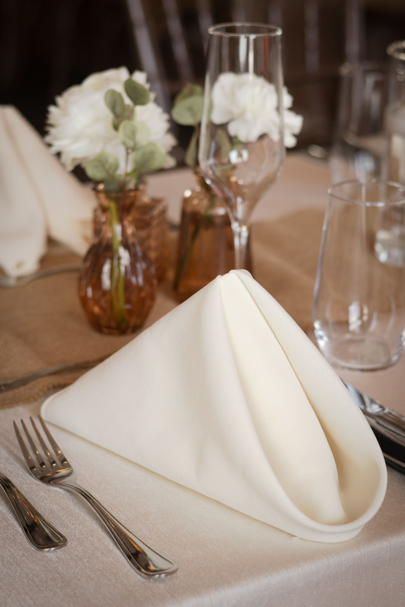 Table setting with folded white napkin, glassware, silverware, and floral arrangement.