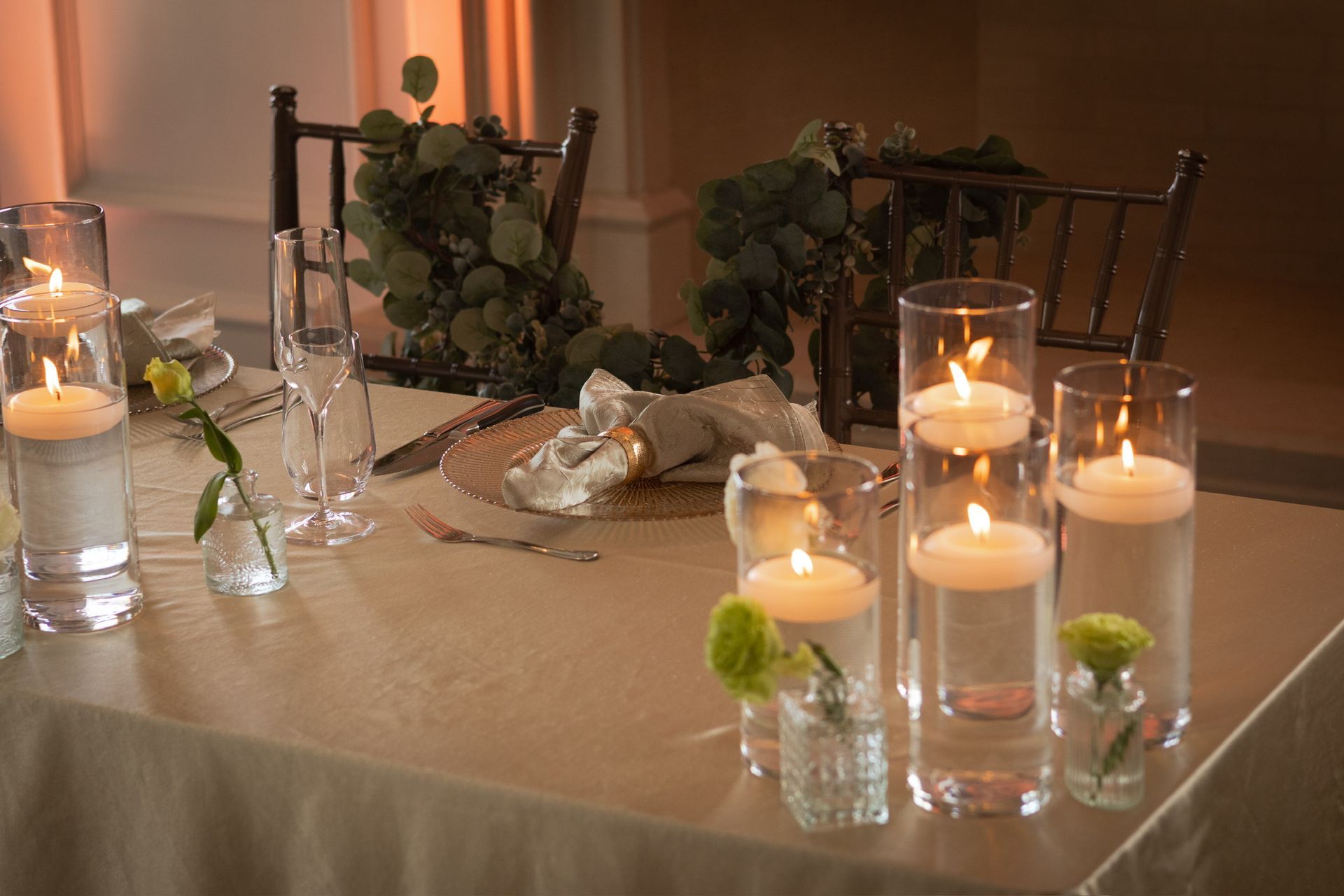Elegant table setting with floating candles in glass cylinders and greenery.