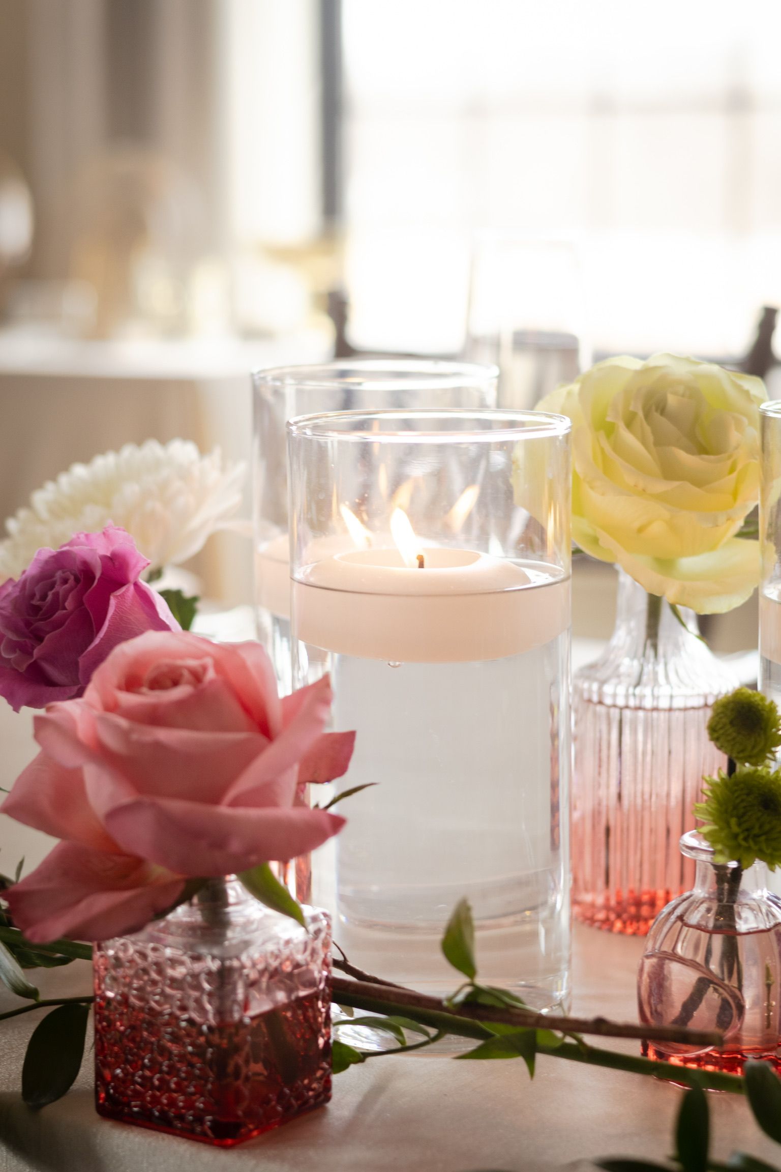 Table setting with floating candle in glass, surrounded by flowers in small vases.