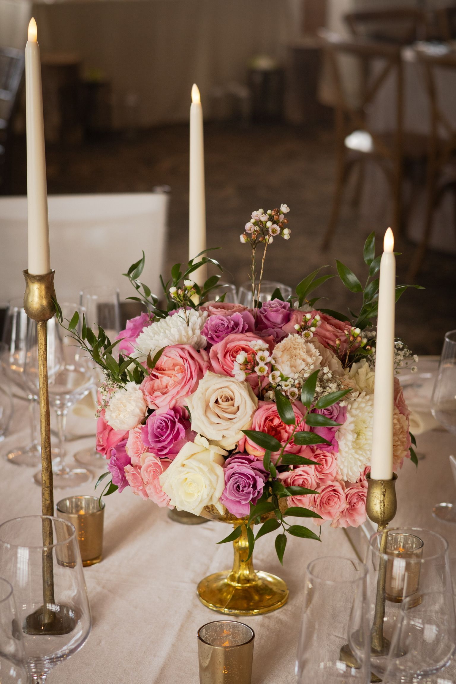 Floral centerpiece with pink and white roses, candles in gold holders on a table.