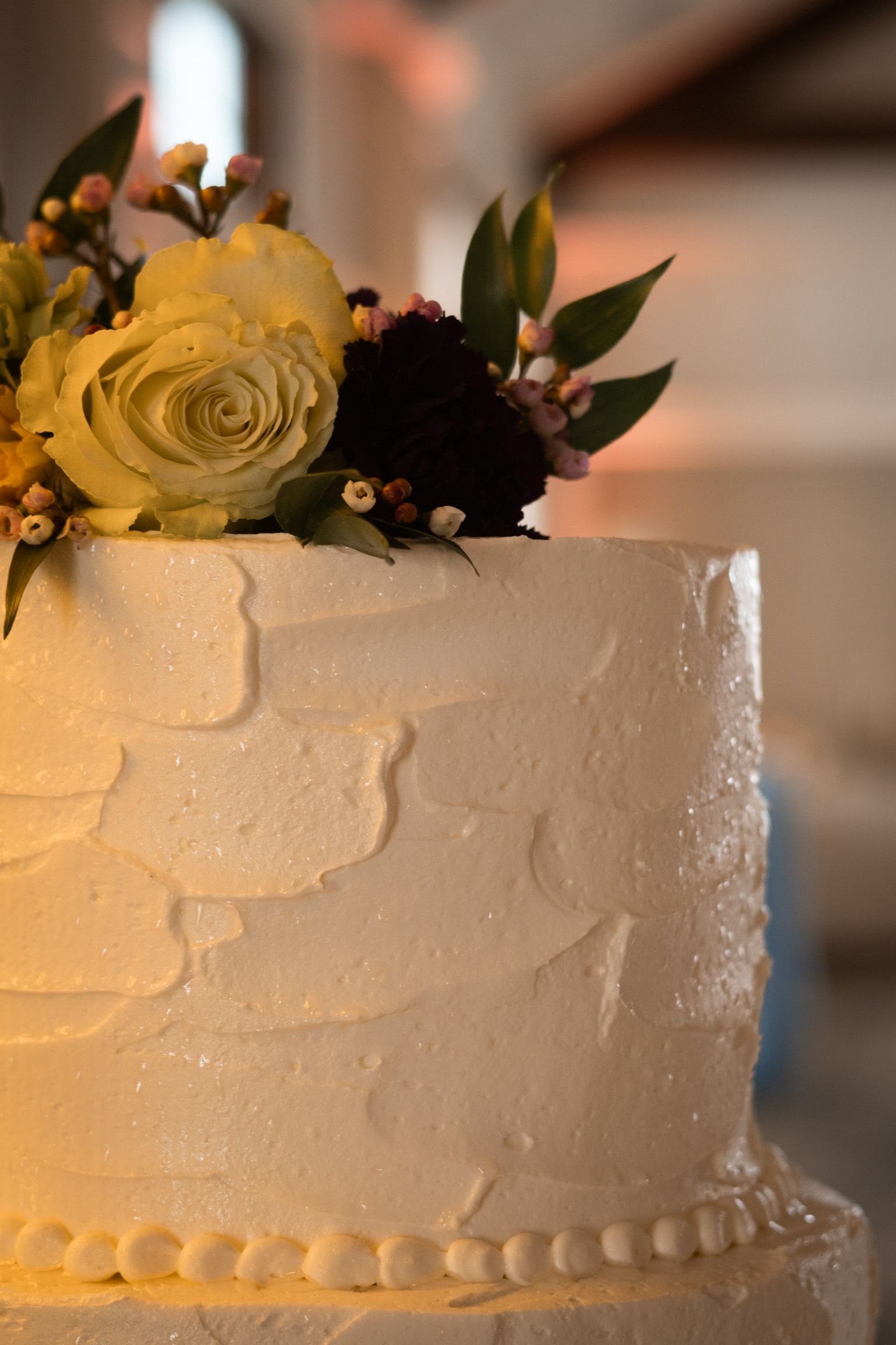 White tiered cake with textured frosting, topped with flowers and greenery.
