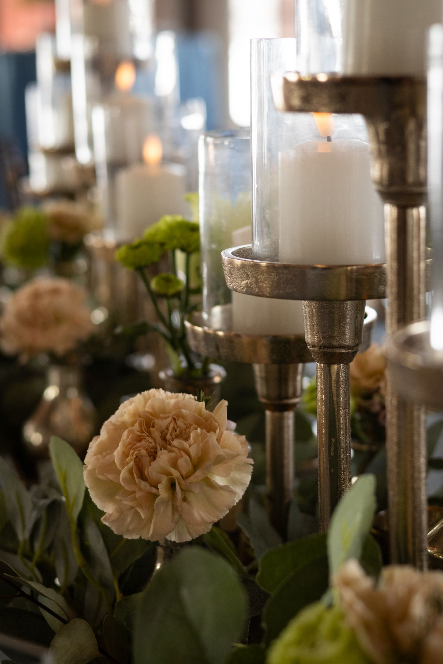 Candles in golden holders amidst flowers and greenery on a table.