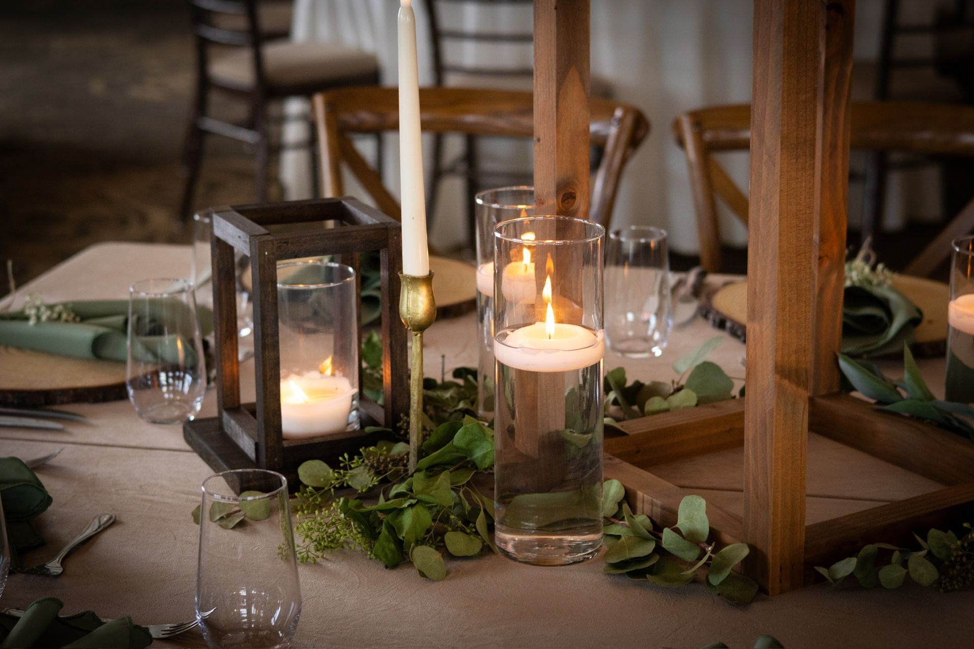 Table setting with wooden lantern, floating candles, greenery, and glassware.