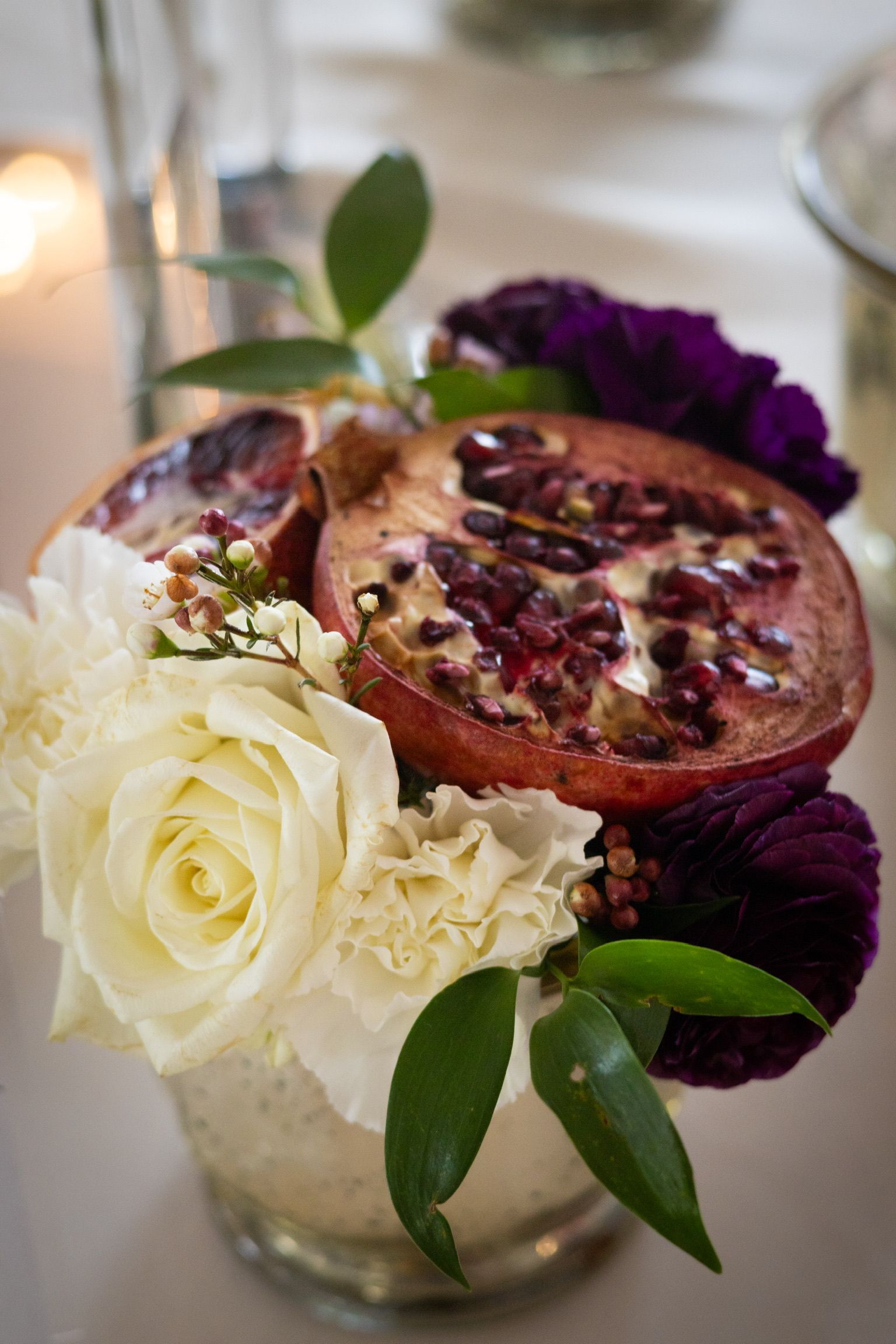 Floral arrangement with sliced pomegranate, white roses, purple flowers, and greenery.