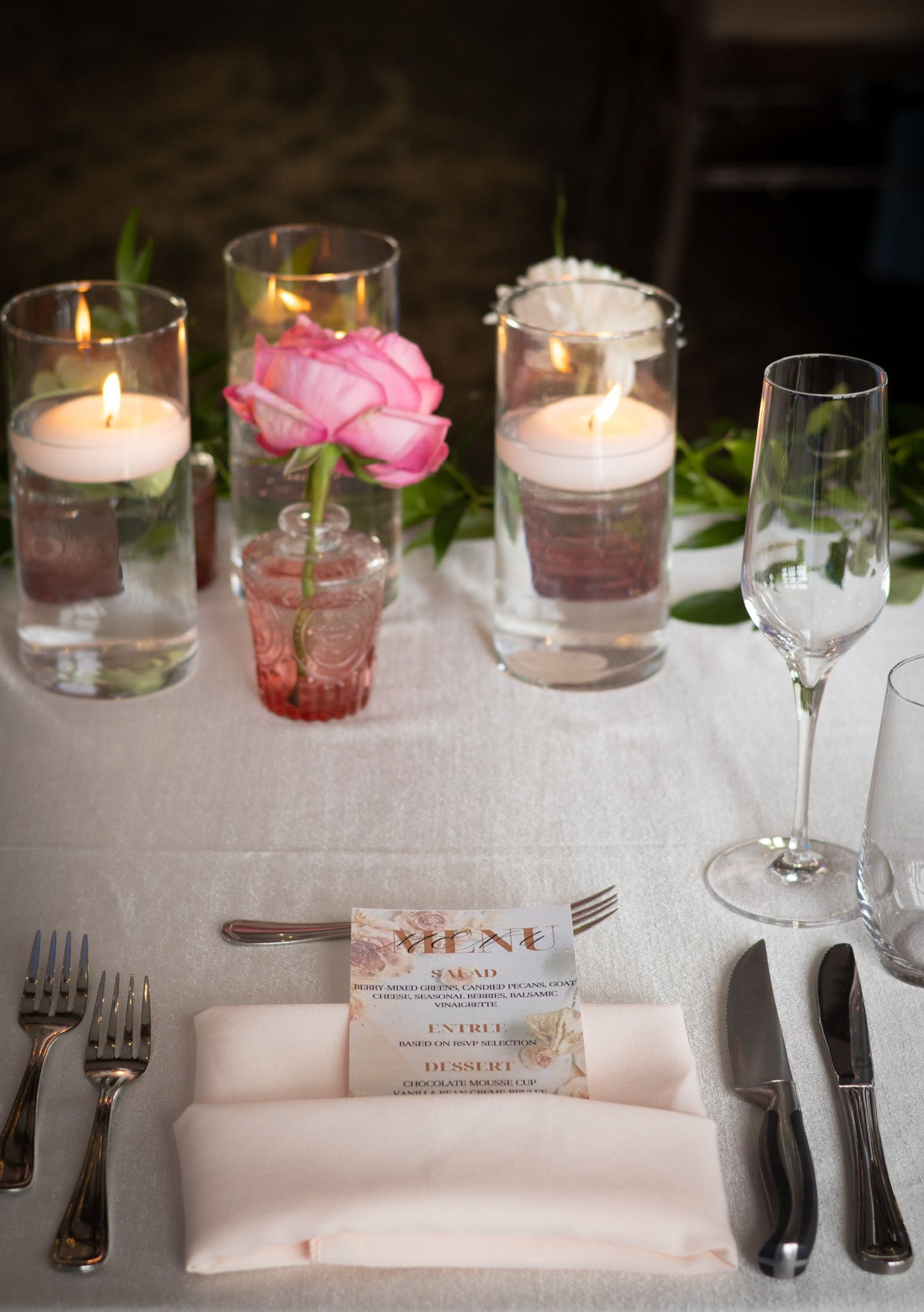 Elegant table setting with floral centerpieces, floating candles, and silverware.