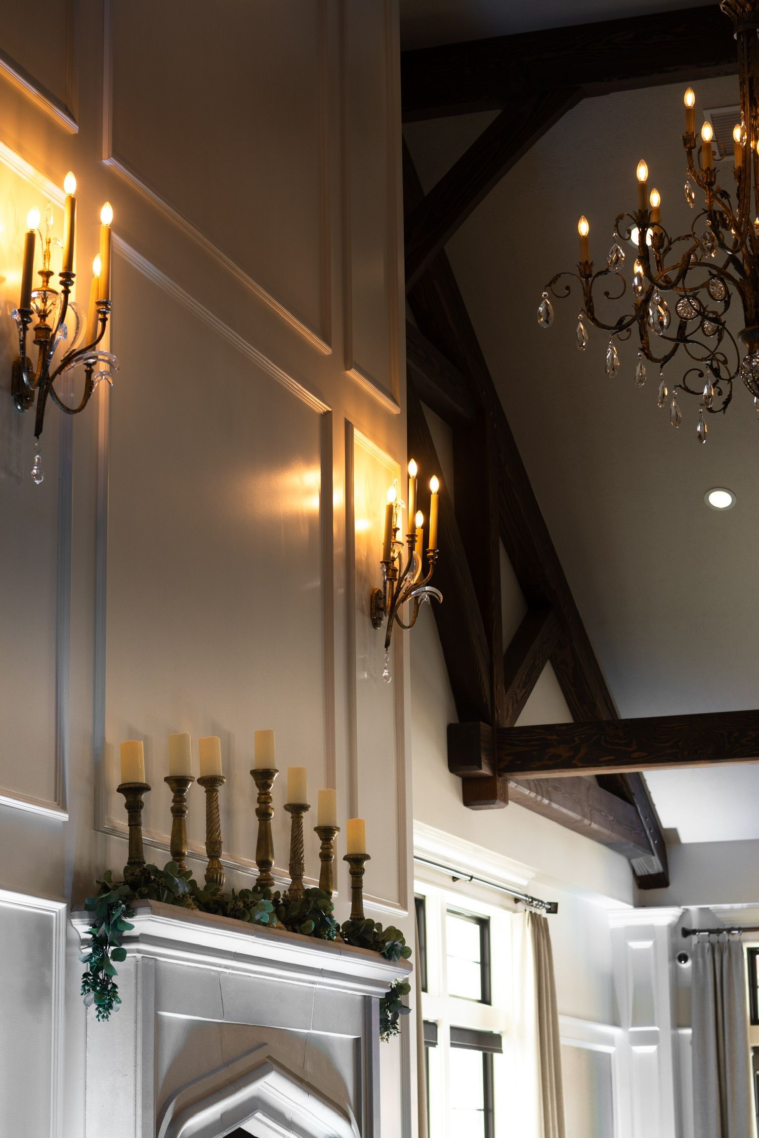 Elegant interior with wall sconces and candles above a fireplace, illuminated by soft light.
