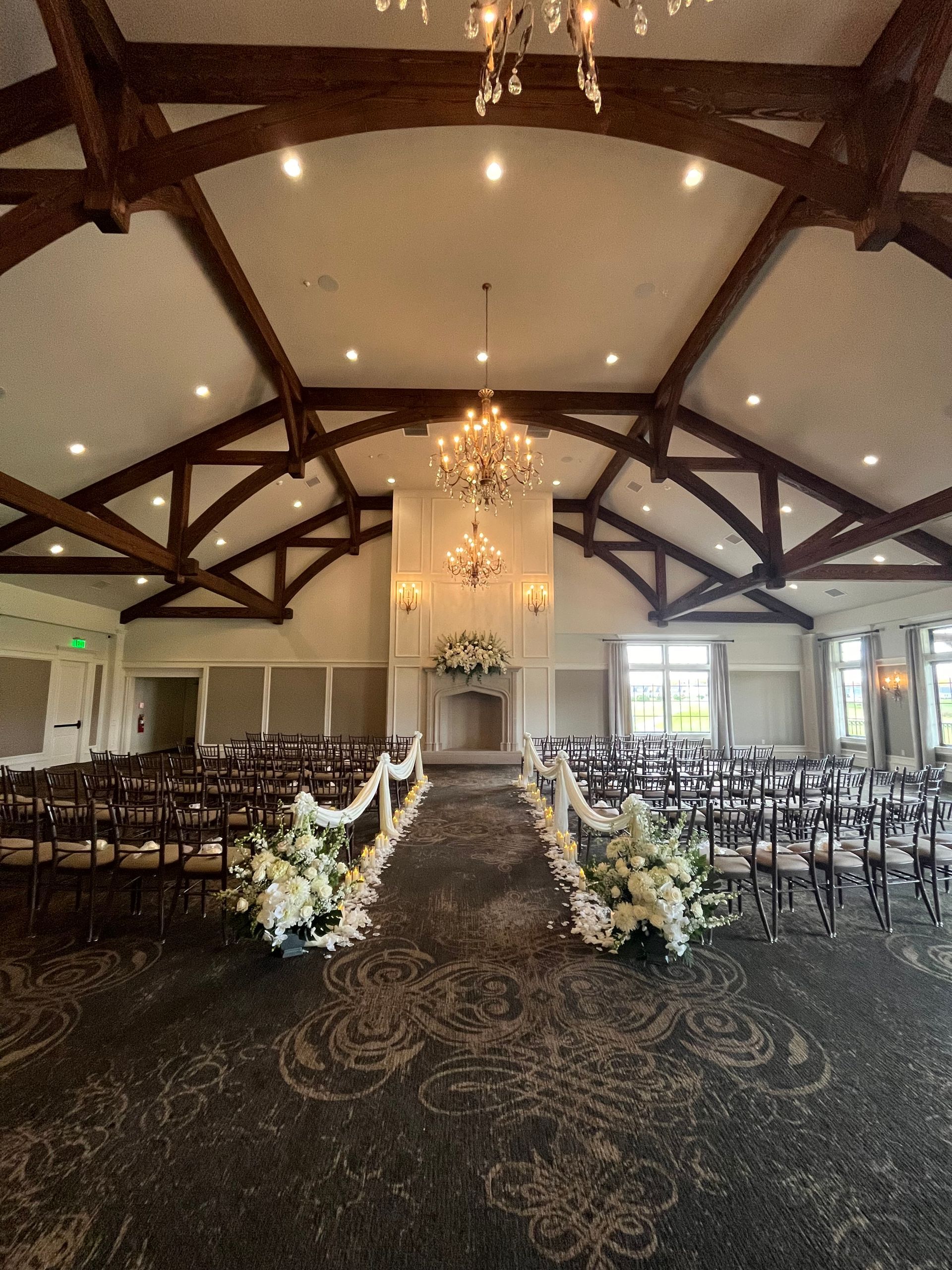 Wedding ceremony setup in a hall with floral aisle decorations, chandeliers, and rows of chairs.