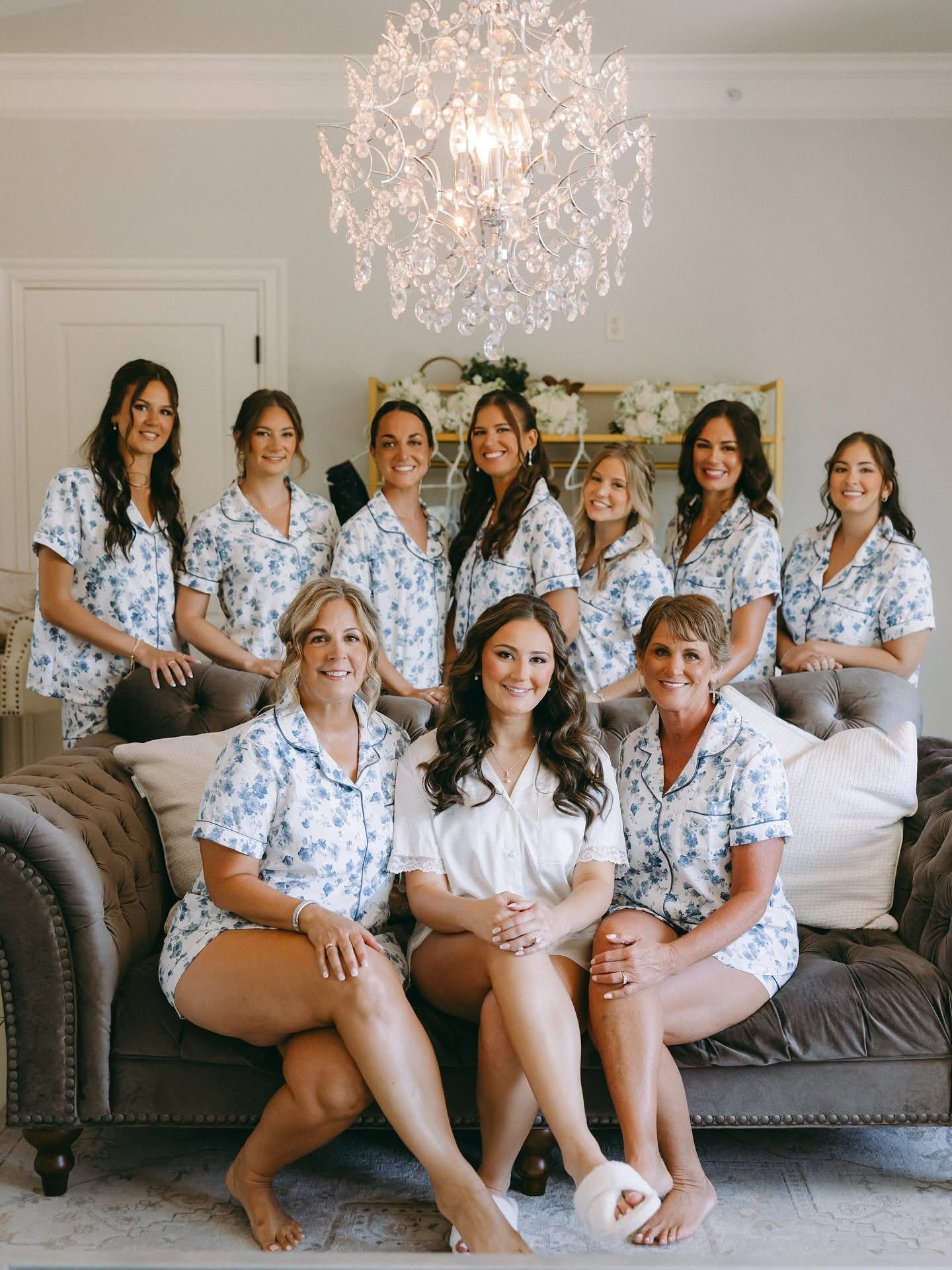 Bridesmaids in matching floral pajamas pose with the bride on a couch in a well-lit room.