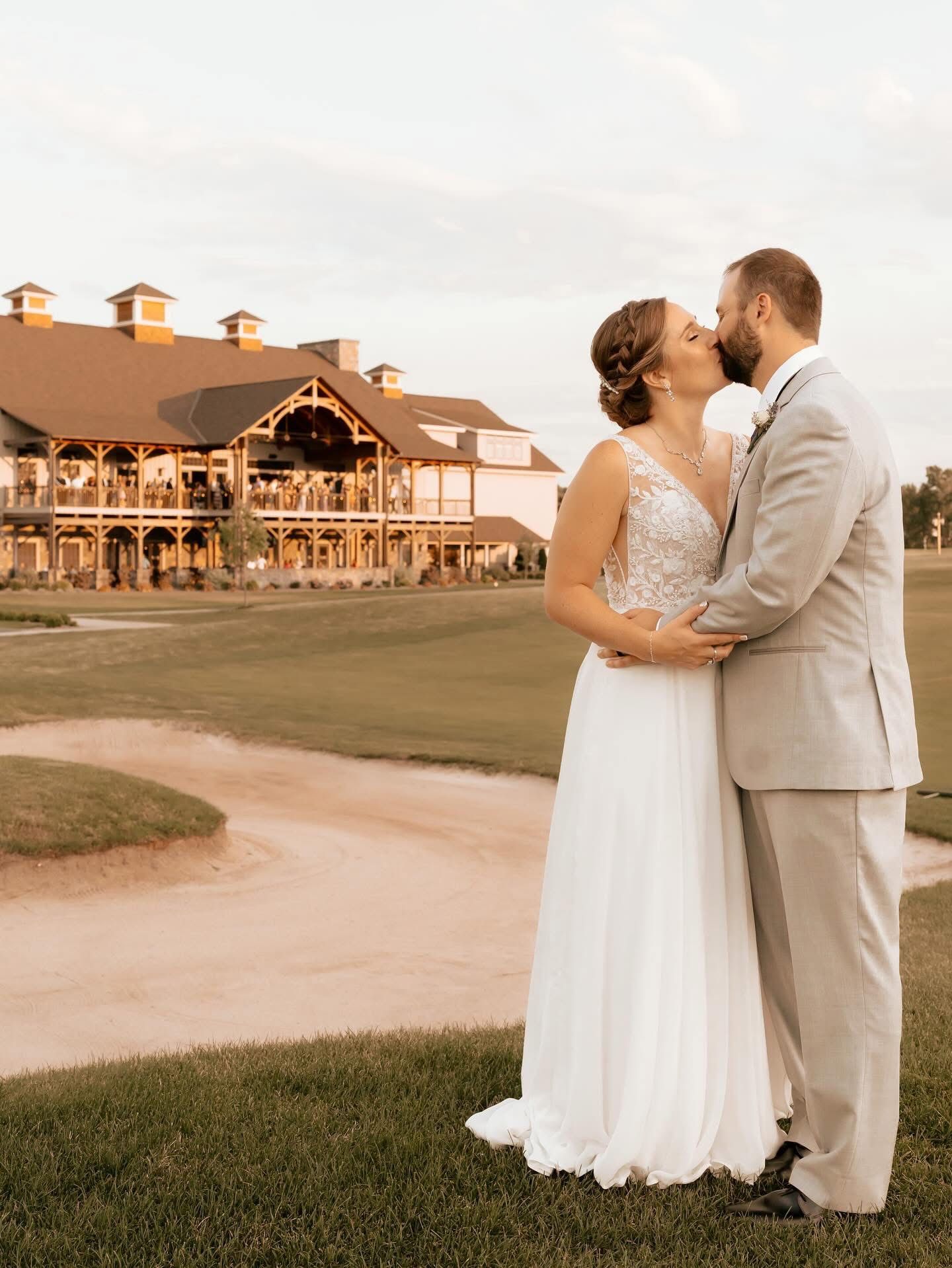 Bride and groom kissing on golf course with large building in background.