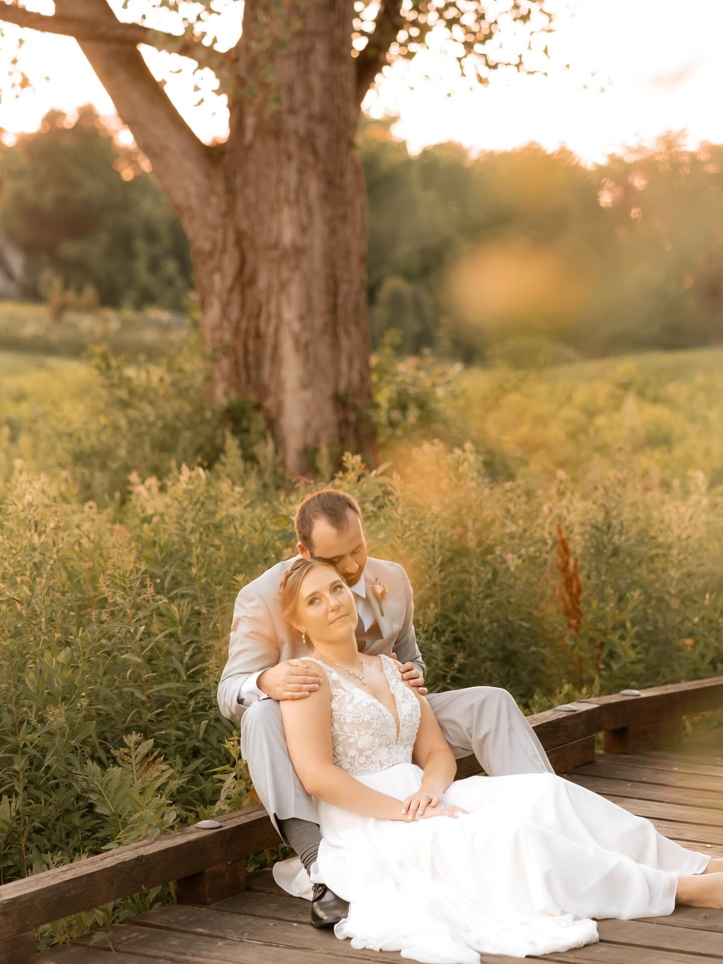 Couple in wedding attire sitting on a wooden walkway, backlit by golden sunlight.