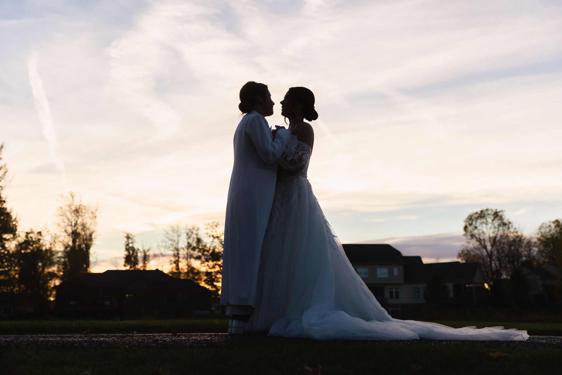 Couple embraces in silhouette against a sunset, woman in a wedding dress.