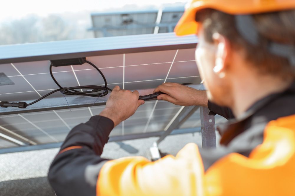 Man In An Orange Hard Hat Is Working On A Solar Panel — Mingleford Electrical Airconditioning Solar & Gas In Kilcoy, QLD