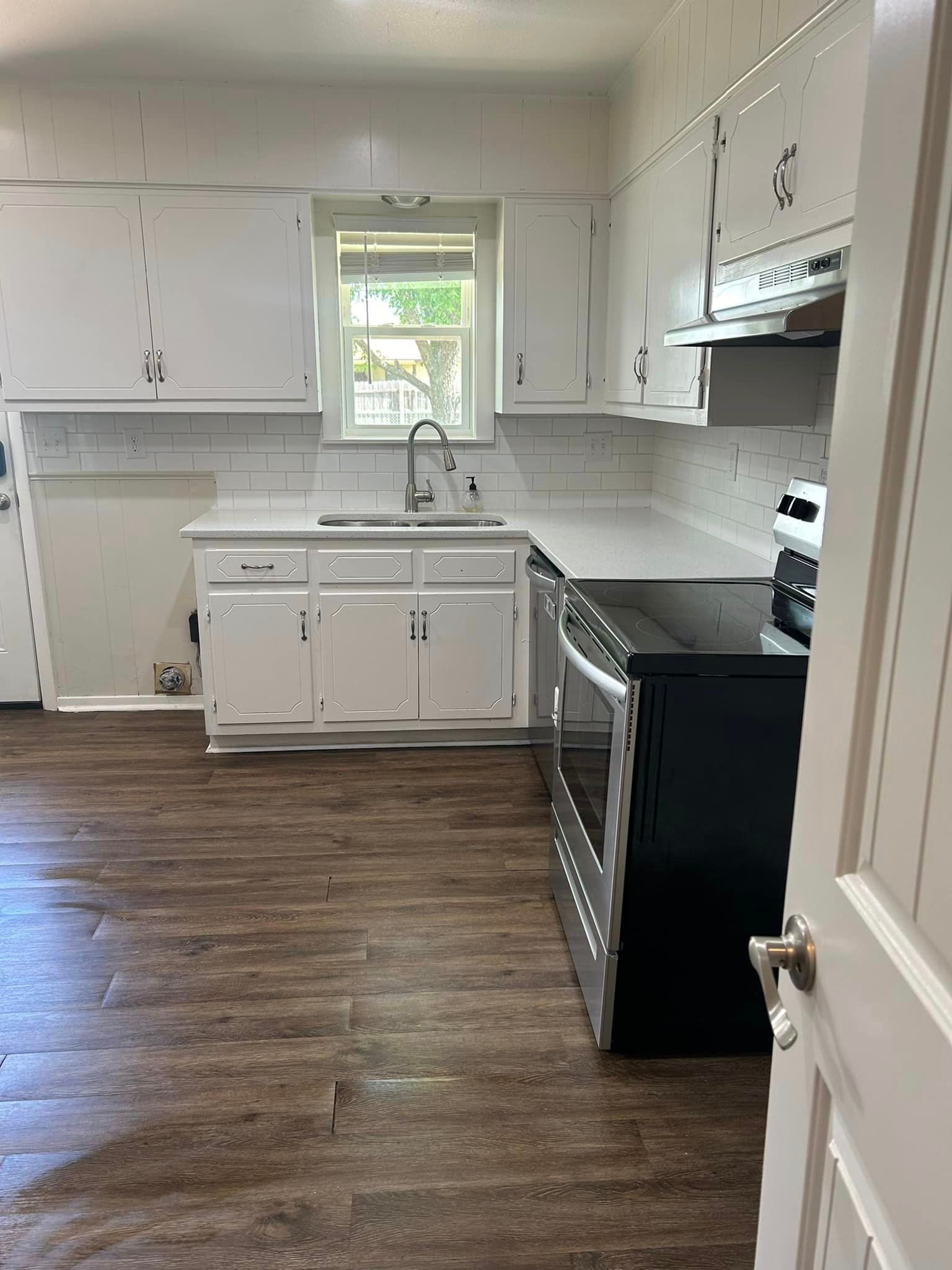 A kitchen with white cabinets , a black stove , a sink , and a window.